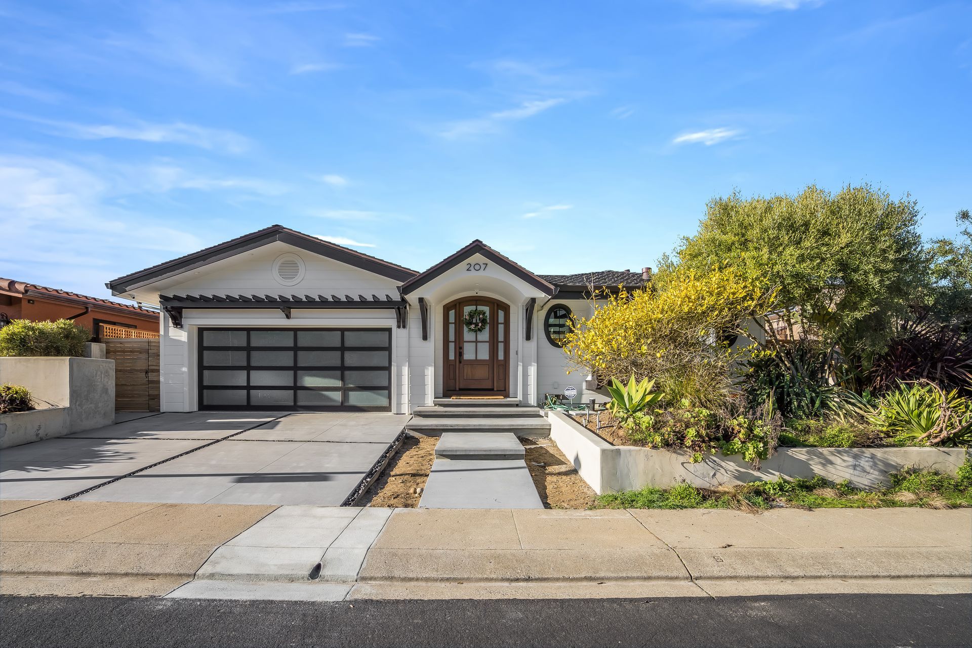 Single-story suburban house with garage, front walkway, and landscaped yard under a blue sky