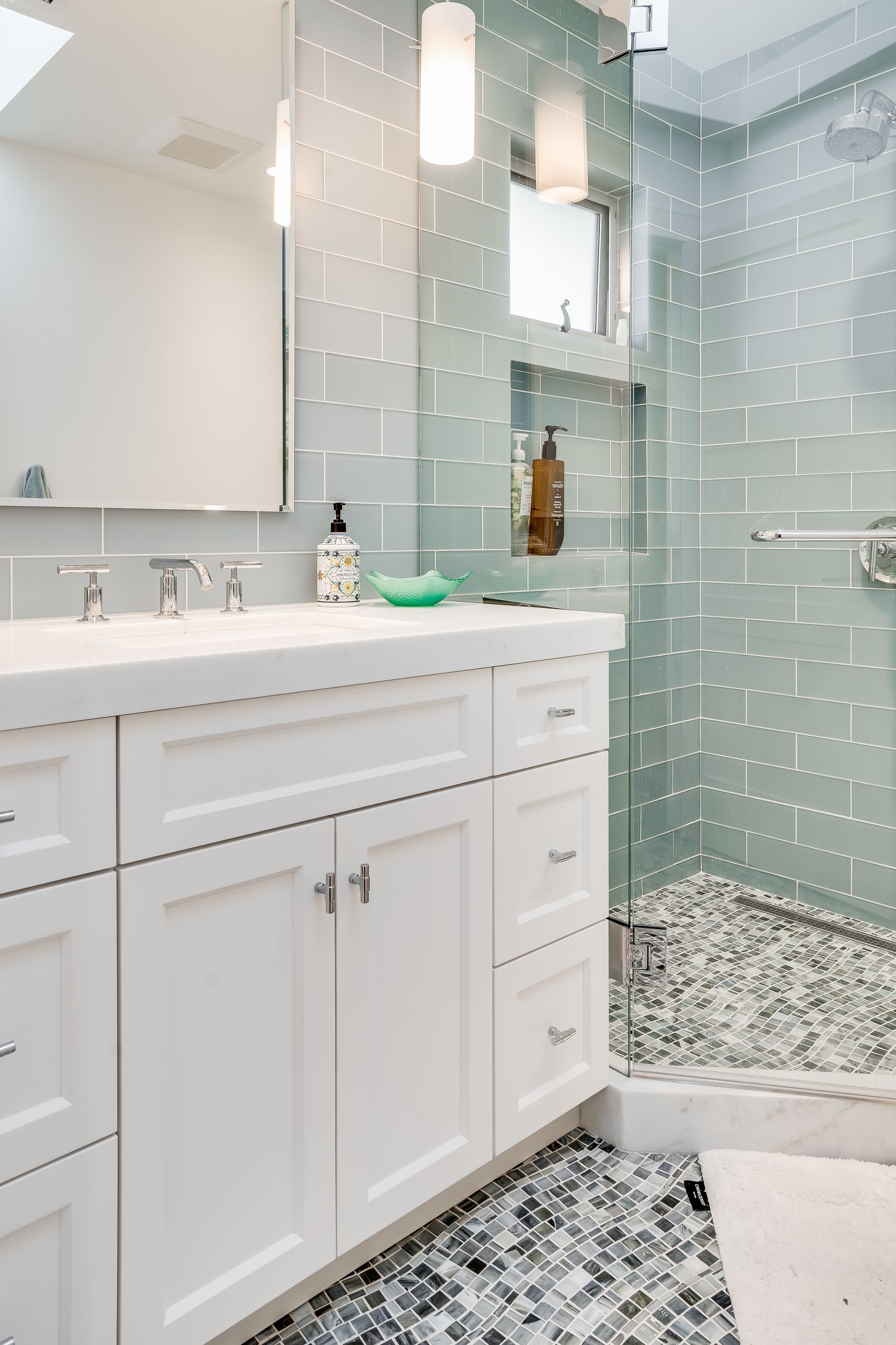 Bright bathroom with white vanity, glass shower, and gray pebble tile floor with mint subway walls