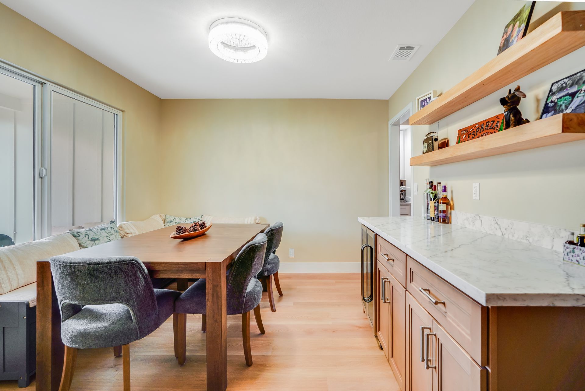 Bright dining room with a long table, gray chairs, built-in cabinets, and wall shelves with decor.