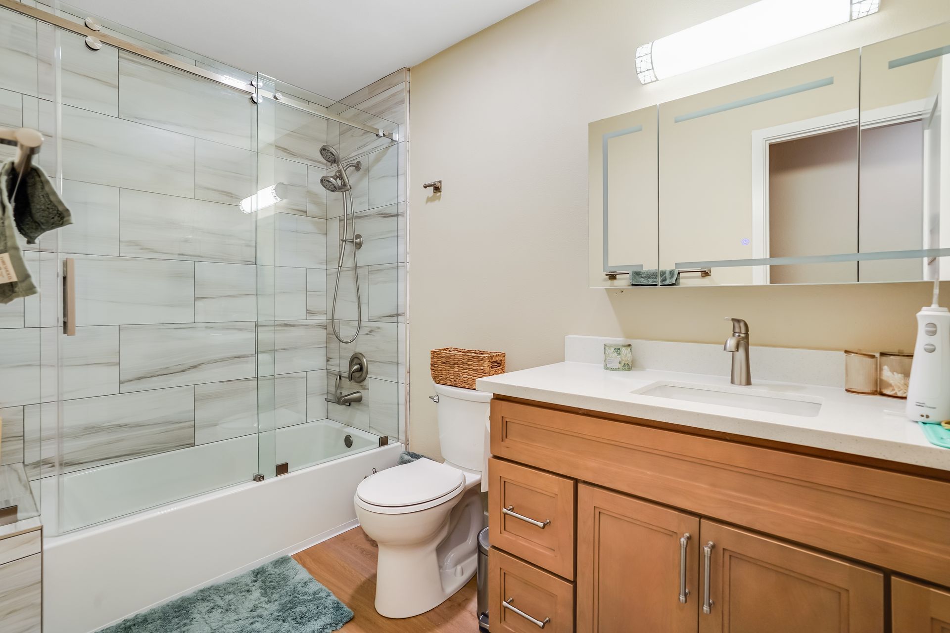 Bright bathroom with glass shower, toilet, wood vanity, and mirror above sink