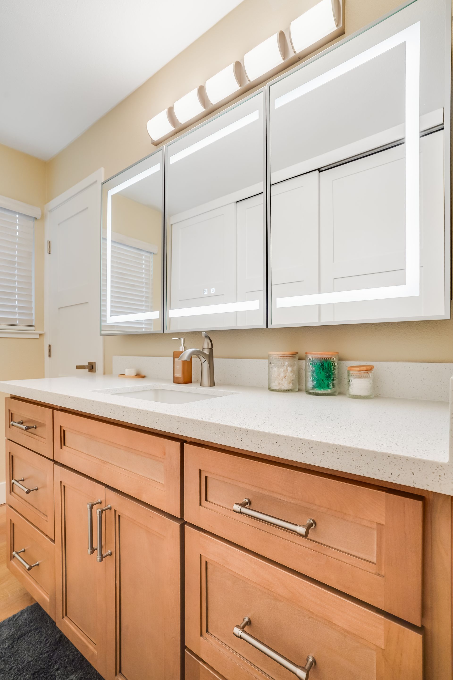 Bright bathroom vanity with white cabinets, large mirror, and granite countertop under vanity lights.