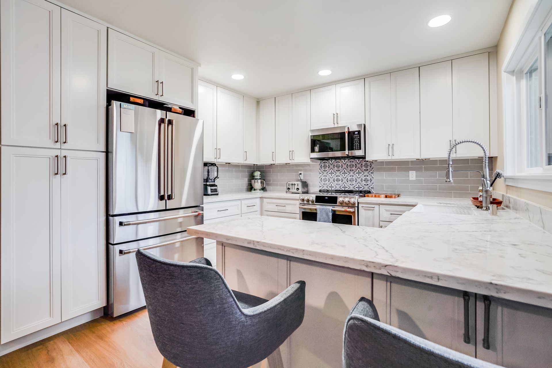 Bright modern kitchen with white cabinets, stainless appliances, and a large marble island with two chairs