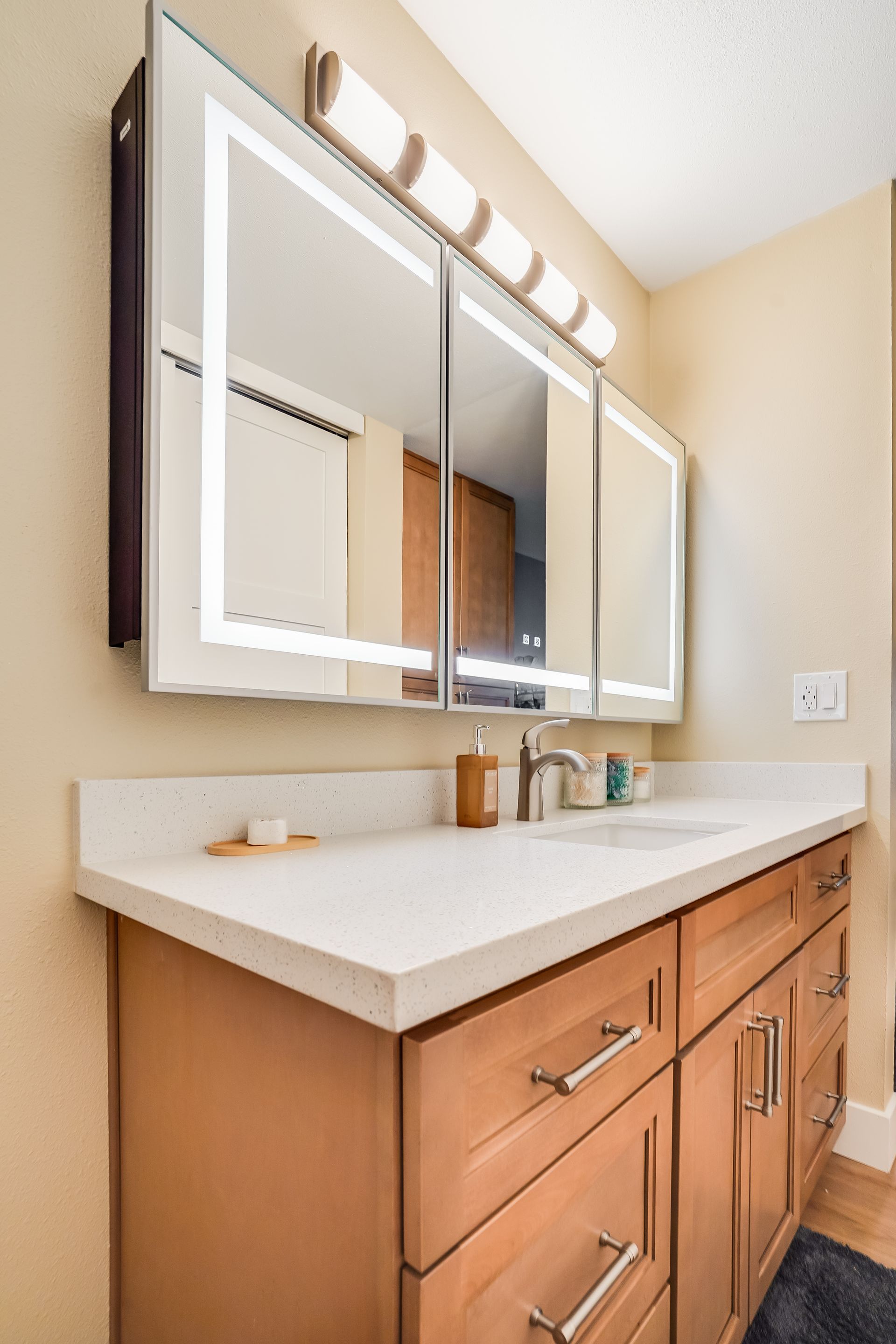 Bathroom vanity with large mirror, lights, white countertop, and wood cabinets.