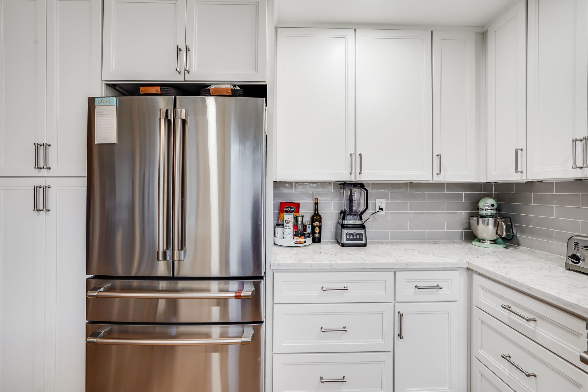 Modern white kitchen with stainless steel refrigerator, cabinets, and countertop appliances