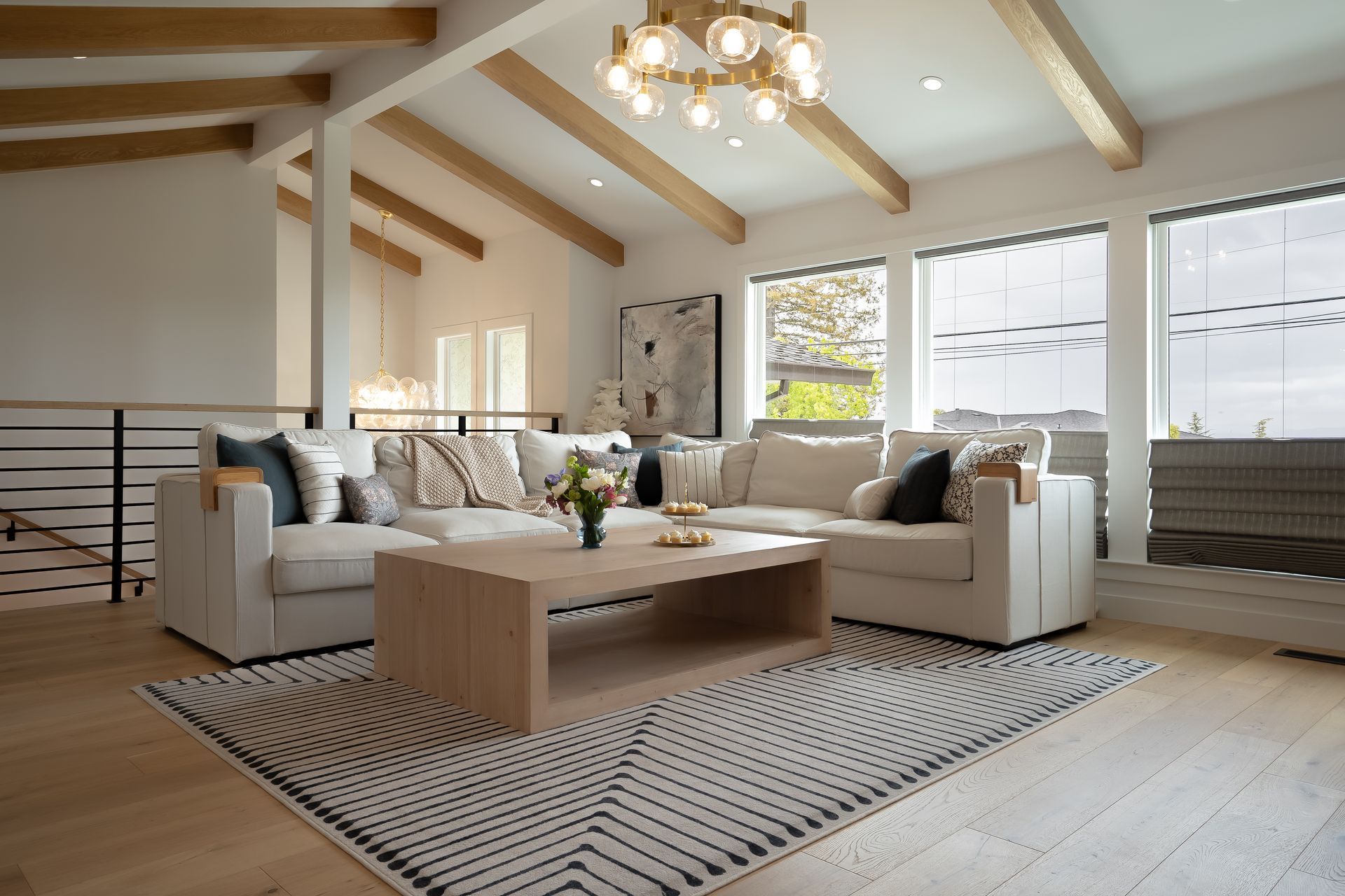 A modern living room with a sectional sofa, area rug, and light wood beams.