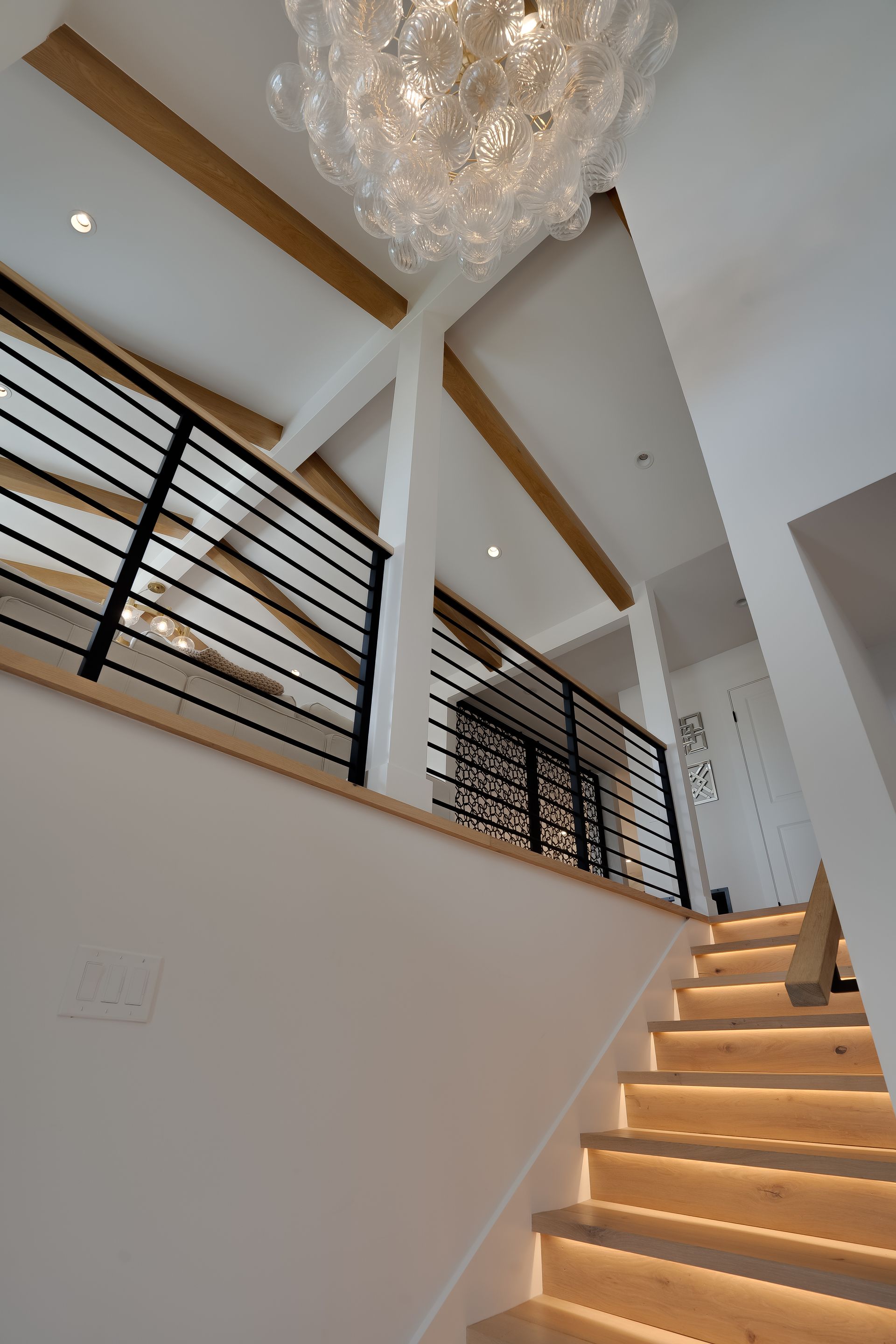 Staircase with lit steps, black railing, white walls, and a bubble-shaped chandelier in a modern home.