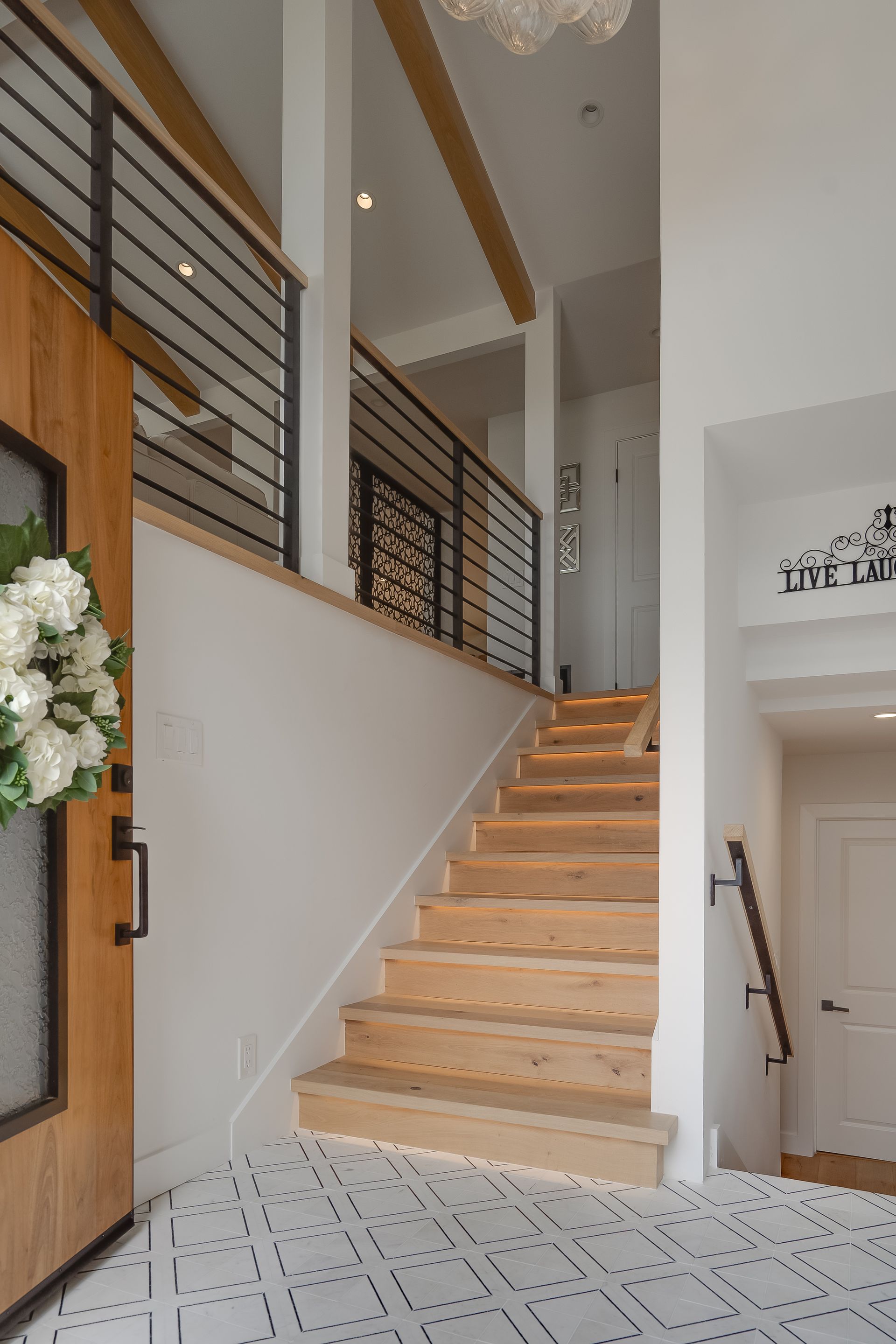 Wooden staircase leading up to a second floor with black railing and wood beams in a bright white interior.