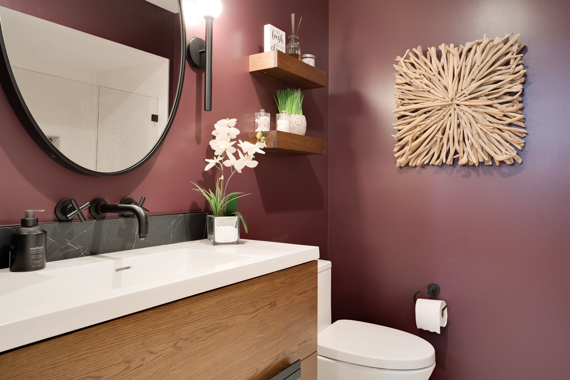 Bathroom with burgundy walls, a white sink, toilet, and decorative wooden shelf with a square driftwood art piece.