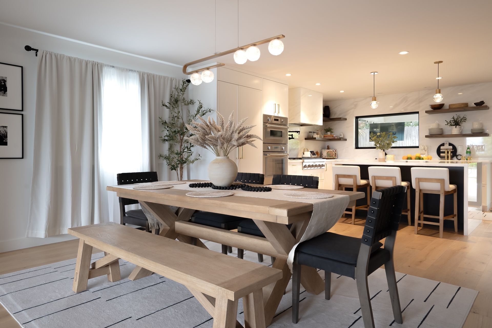 Dining room with light wood table, black chairs, kitchen in background.
