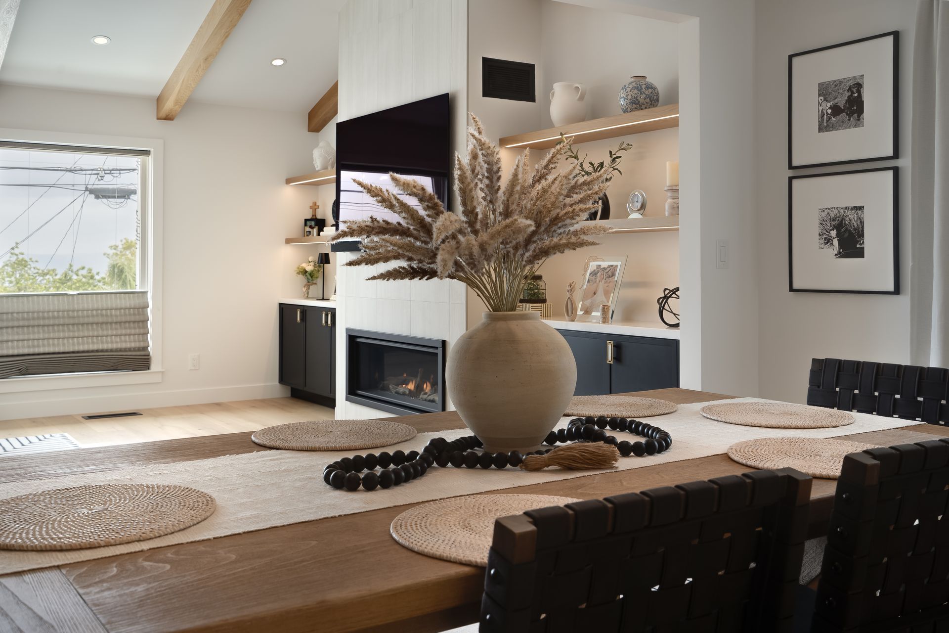 Dining room with dining table, vase, fireplace, TV, and built-in shelves; neutral colors.