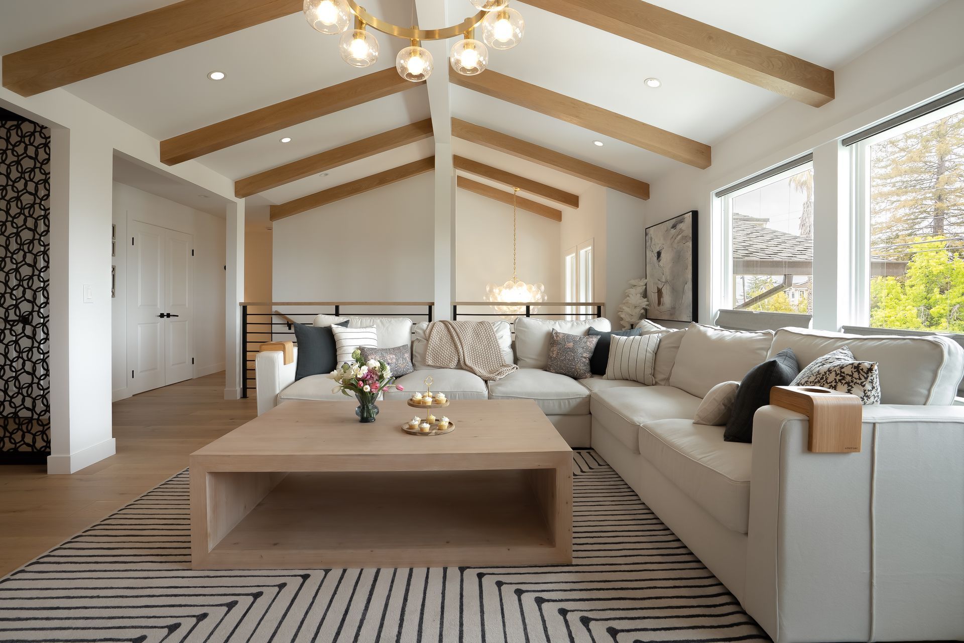 Living room with white sectional sofa, light wood beams, and geometric rug.