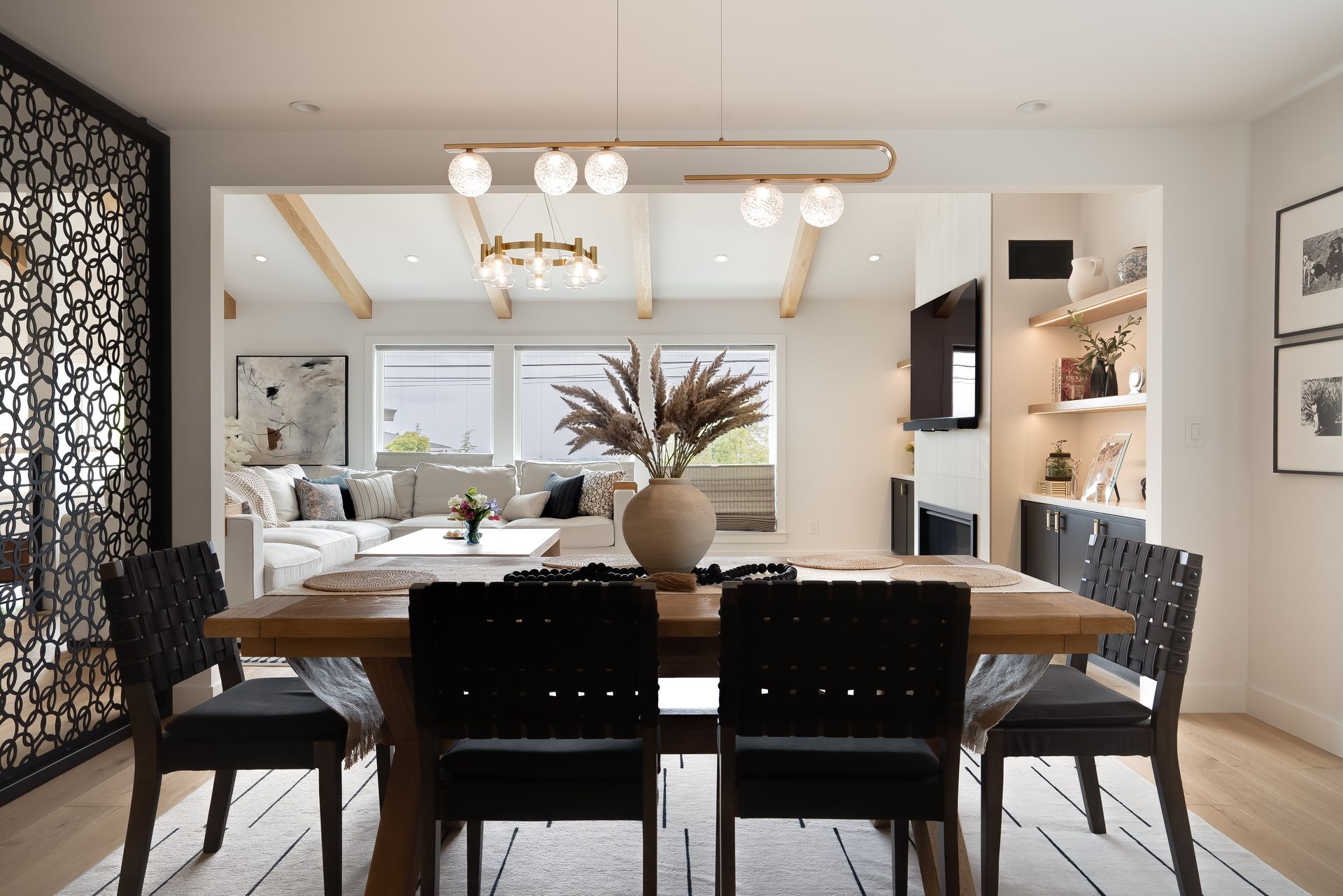 Dining room with wooden table, black chairs, and modern light fixture, with view of living room.