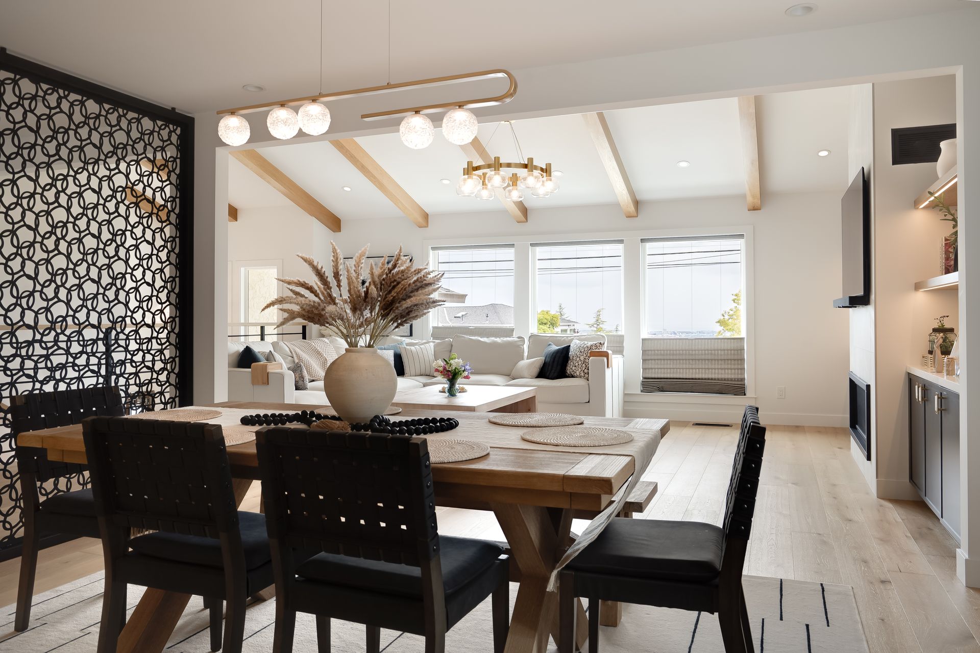 Dining room with wood table, black chairs, and modern lighting; open to a living room with white sofas.
