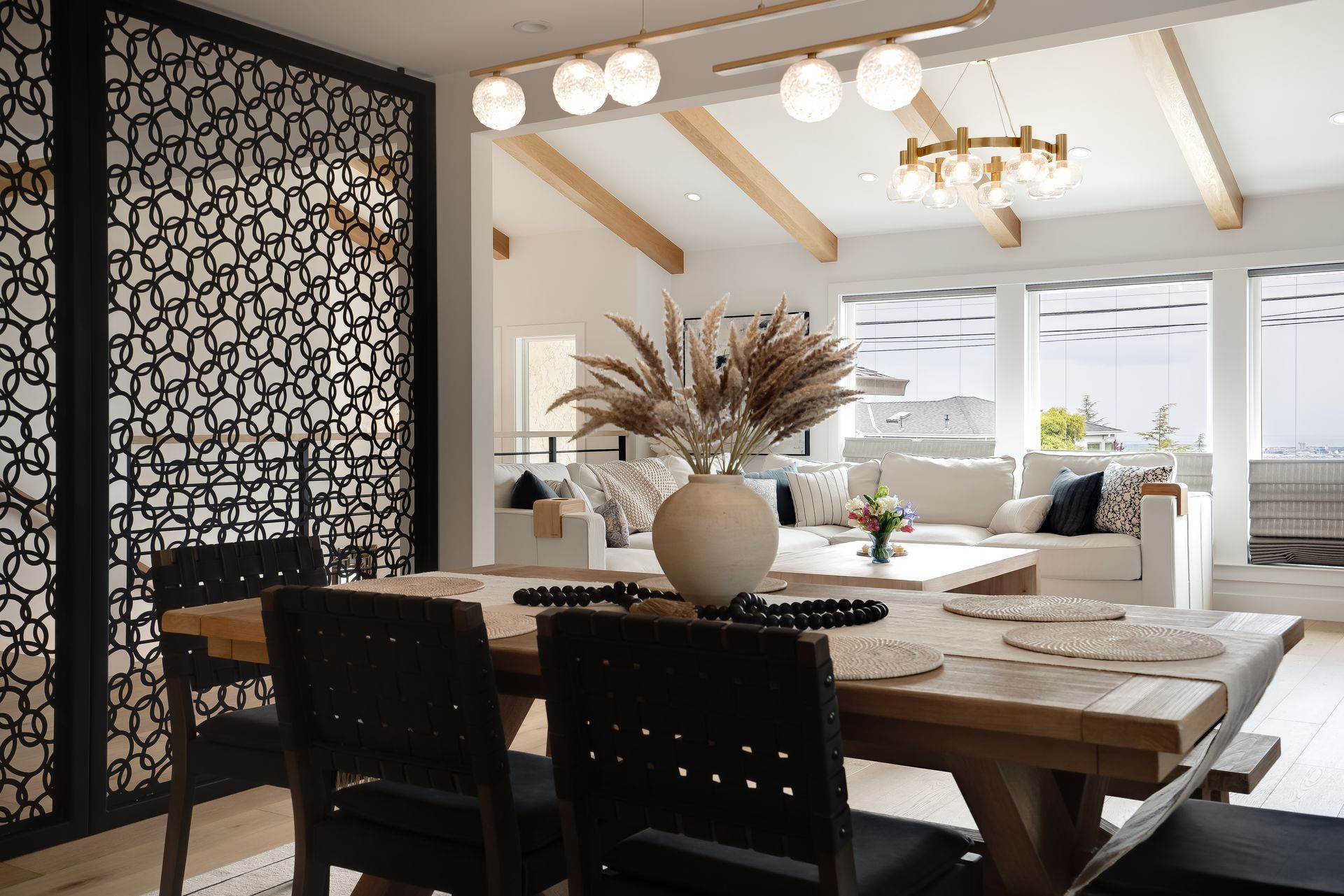Dining room with wood table, black chairs, and decorative screen. White walls and a neutral color scheme.
