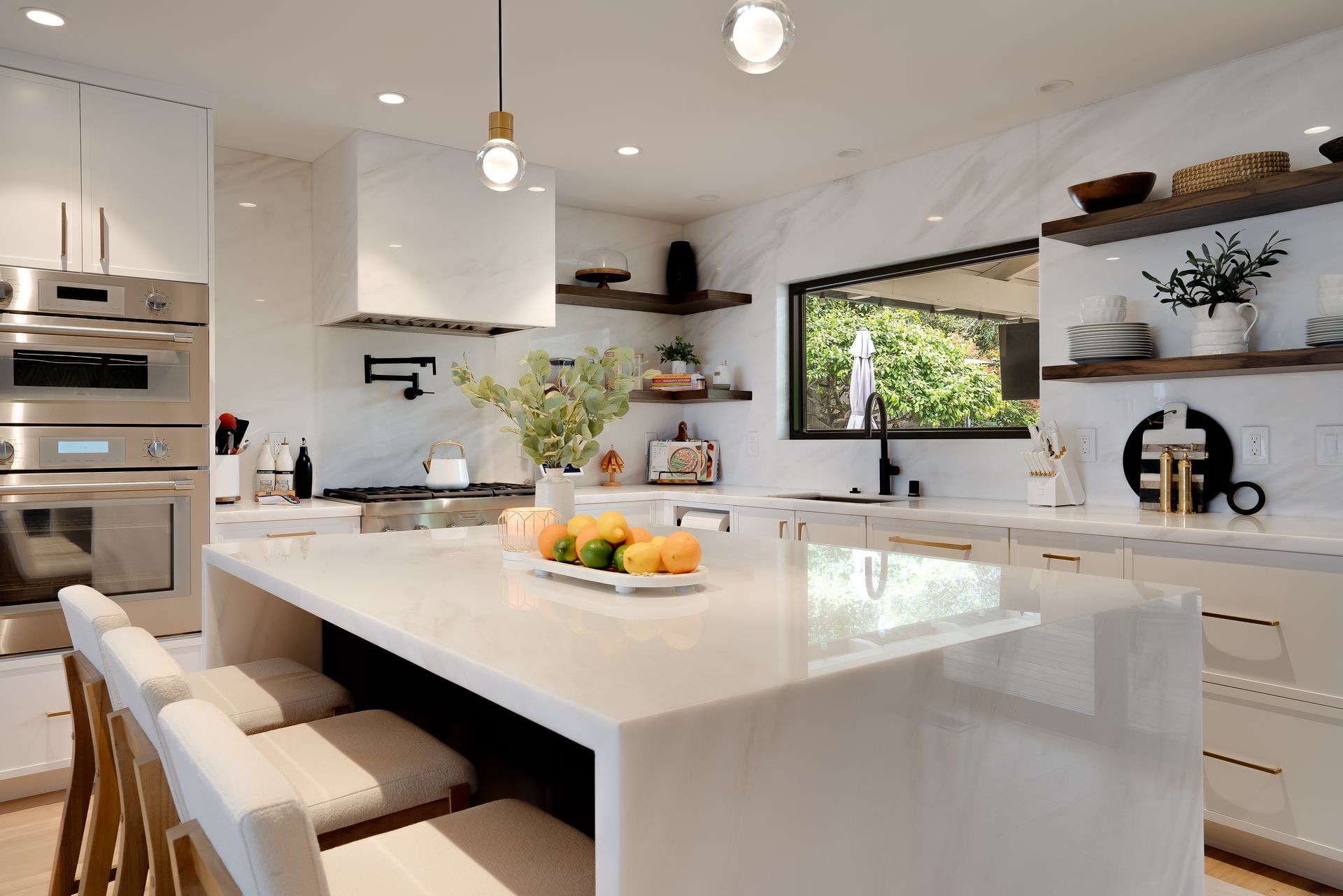 Modern white kitchen with island, marble countertops, and stainless steel appliances.