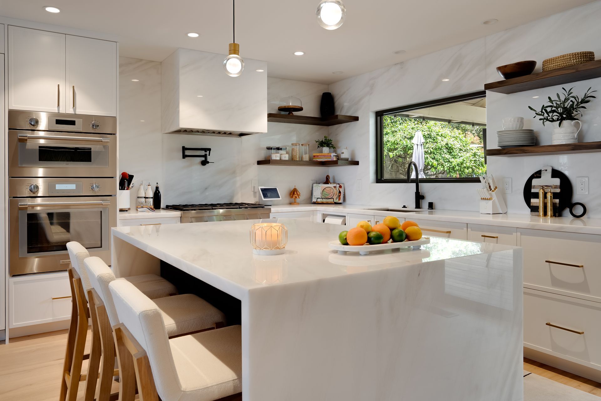 Modern white kitchen with marble countertops, island, and stainless steel appliances.