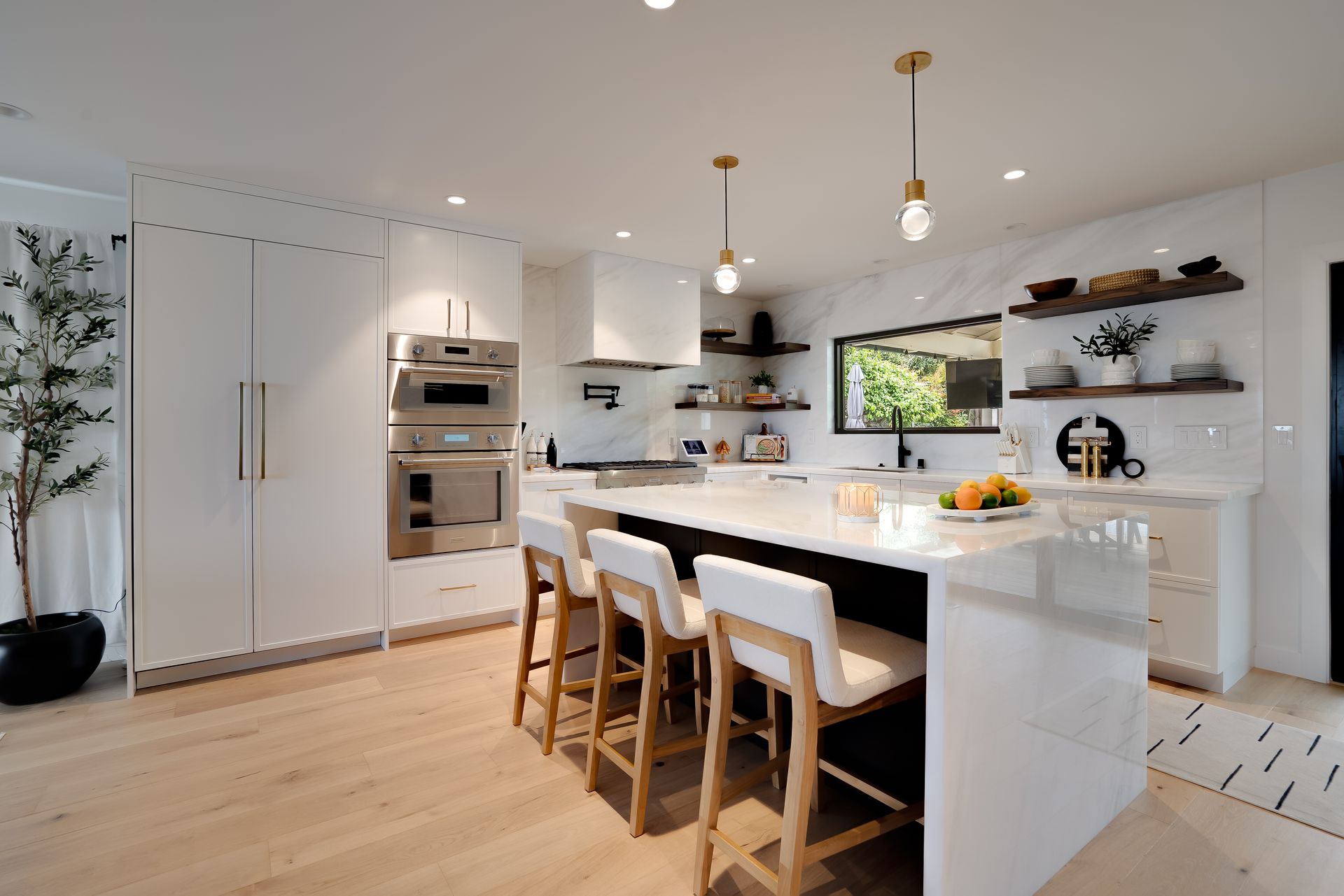 Modern white kitchen with island seating, wood floors, marble backsplash, and black accents.