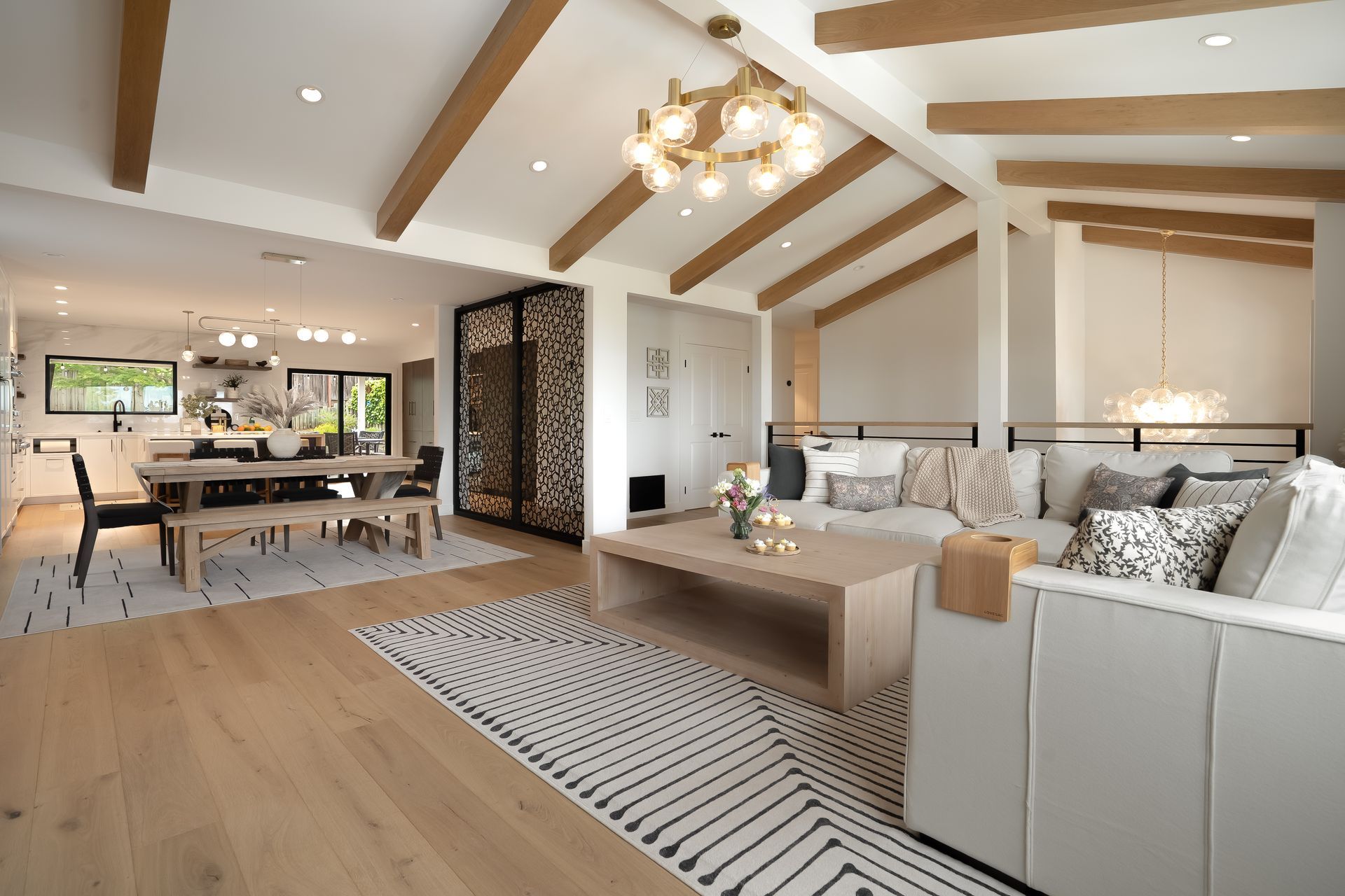 Living room with wood beams, a light-colored couch, and a dining area in a modern home.