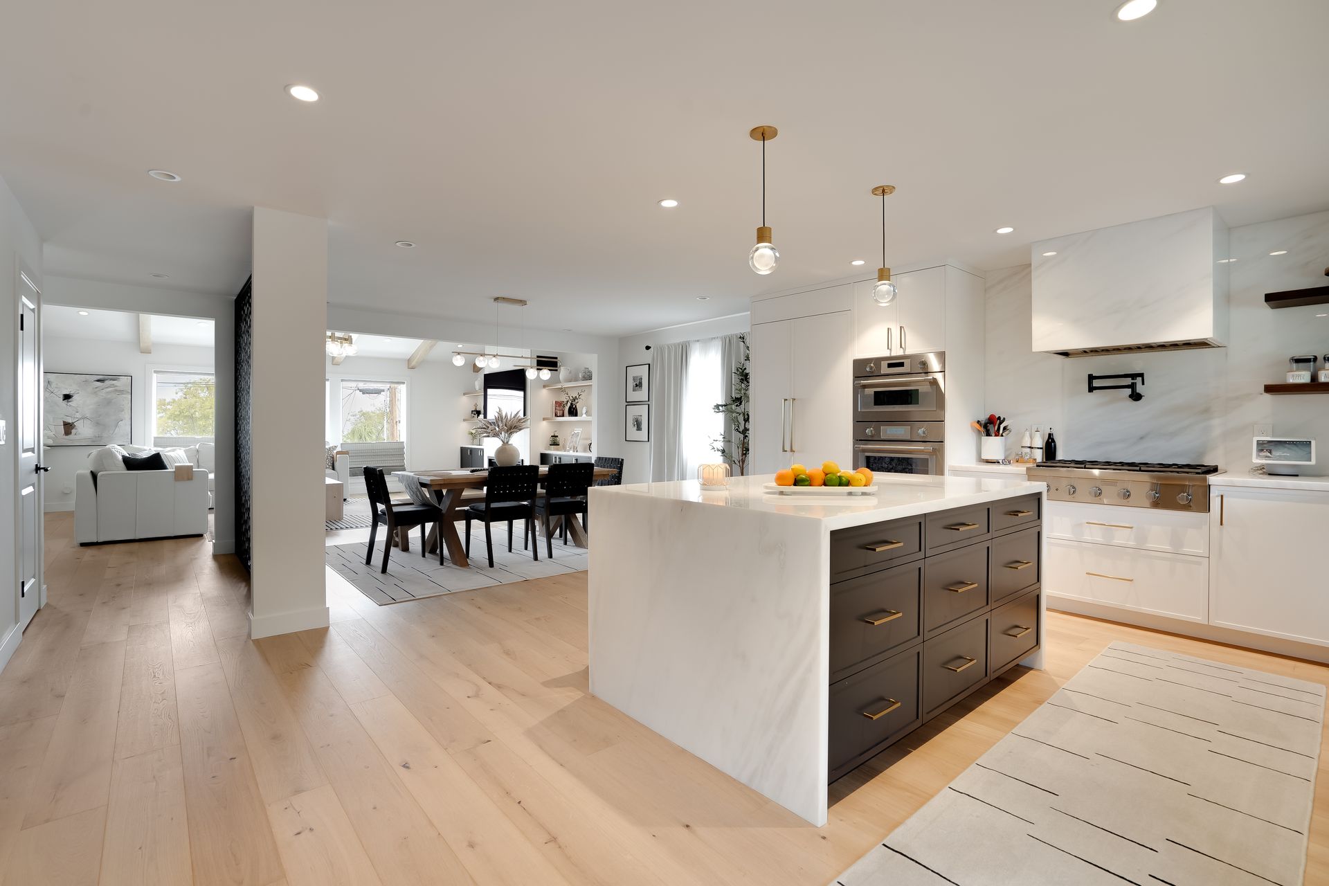 Spacious kitchen with a marble island, dark cabinets, and stainless steel appliances. Open to dining and living areas.