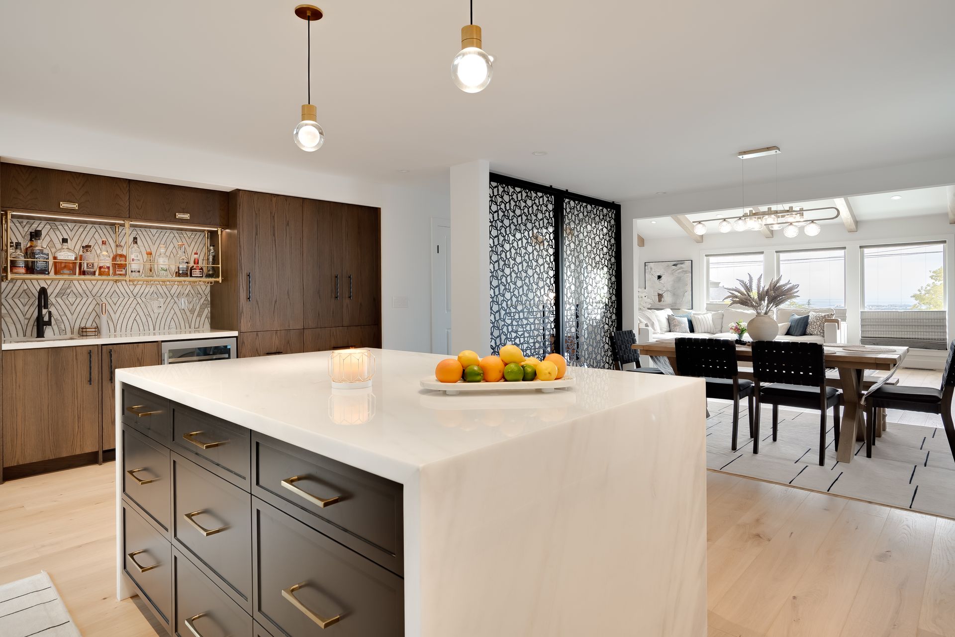 Modern kitchen with island, dark cabinets, and light wood floors. Dining area visible in the background.