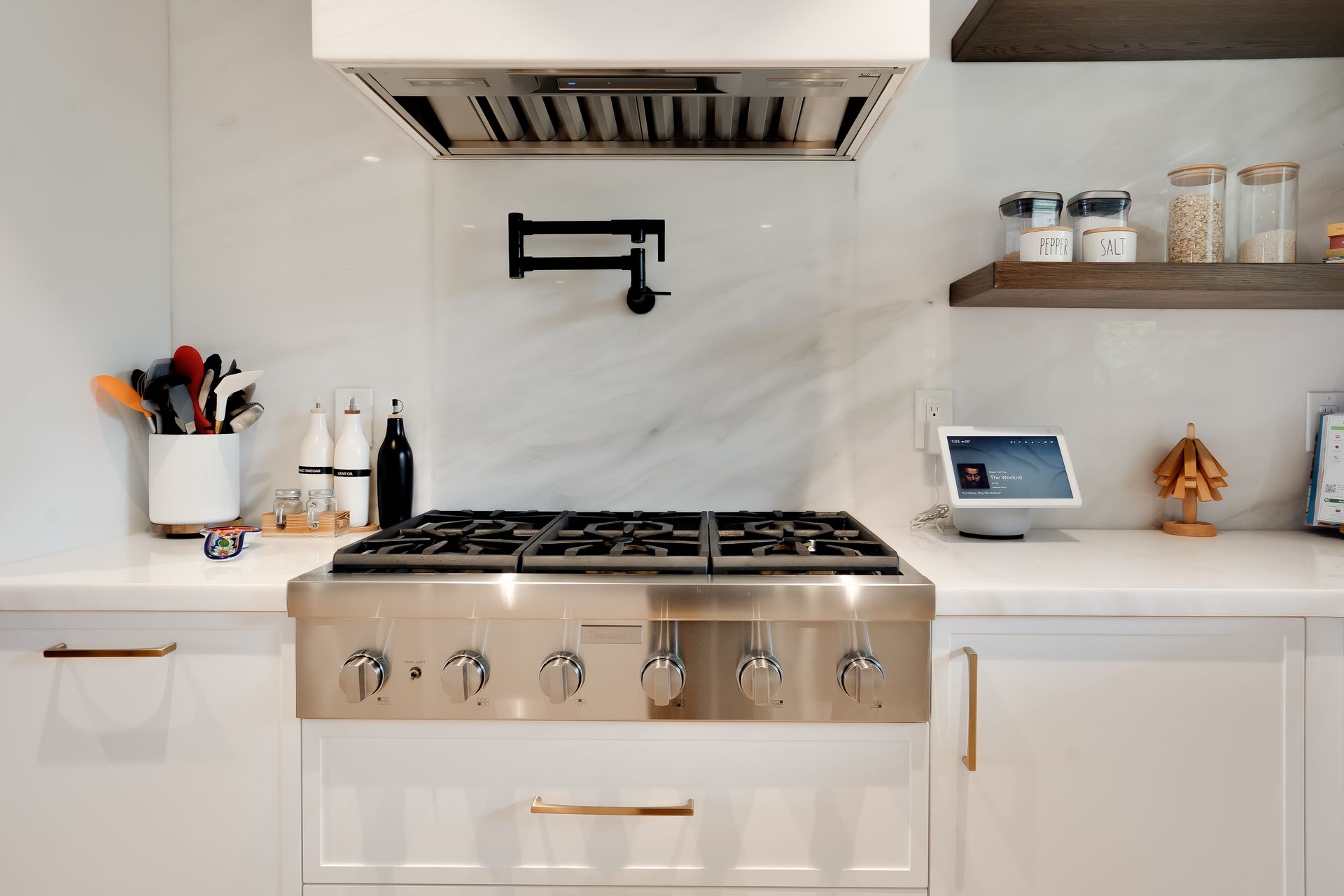 White kitchen with stainless steel range and marble backsplash; pot filler above.