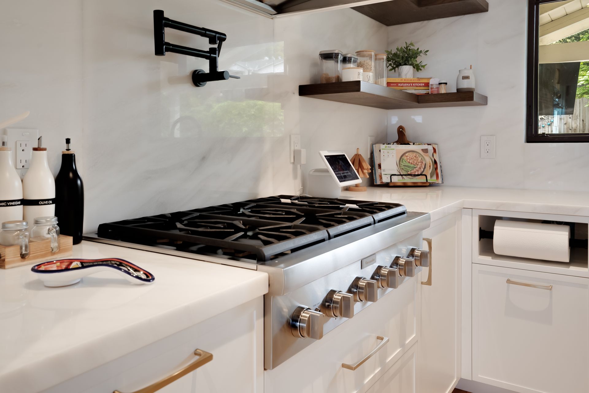 Modern kitchen with white countertops, stove, open shelving, and window.