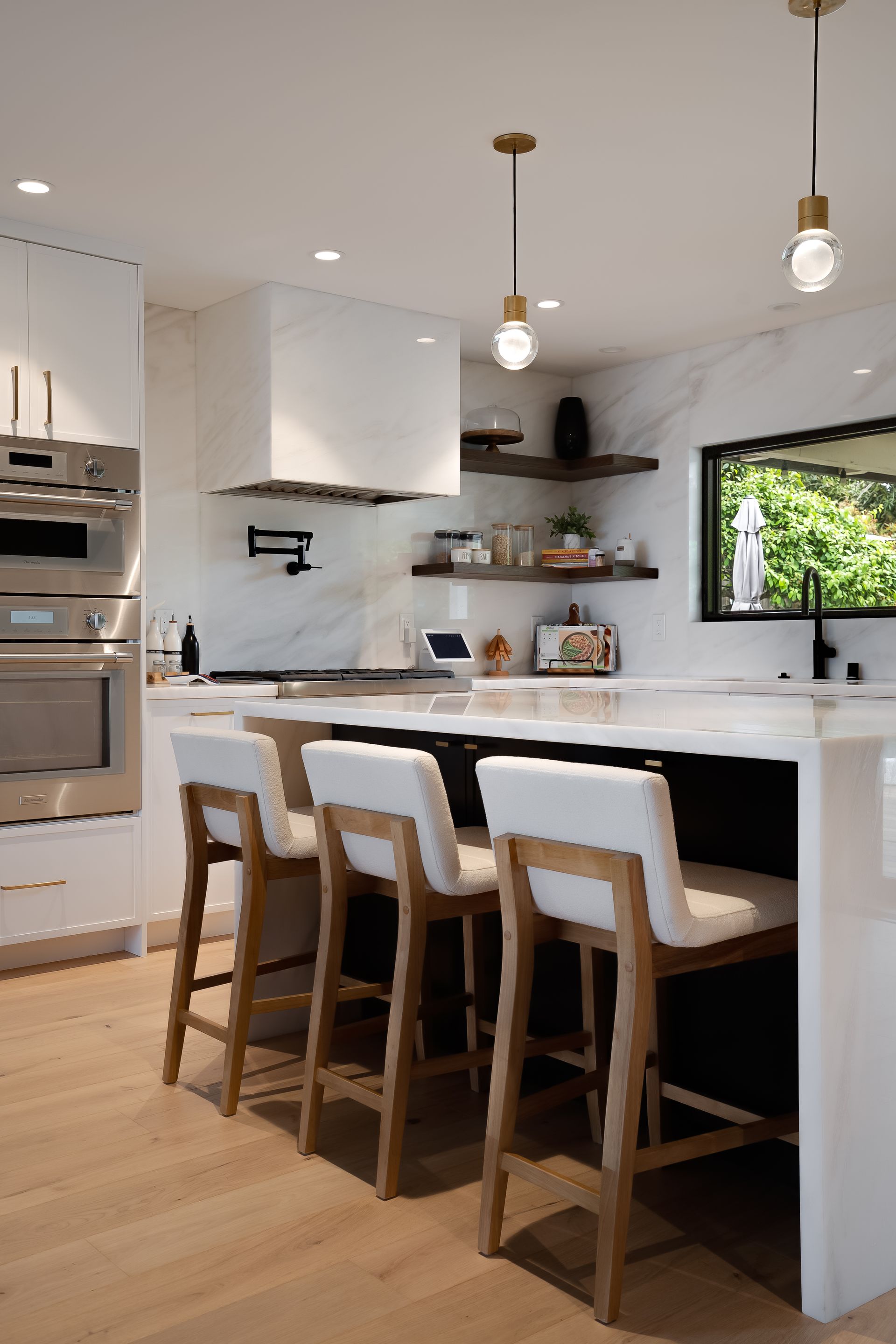 Modern kitchen with white island, wood bar stools, and gold light fixtures.