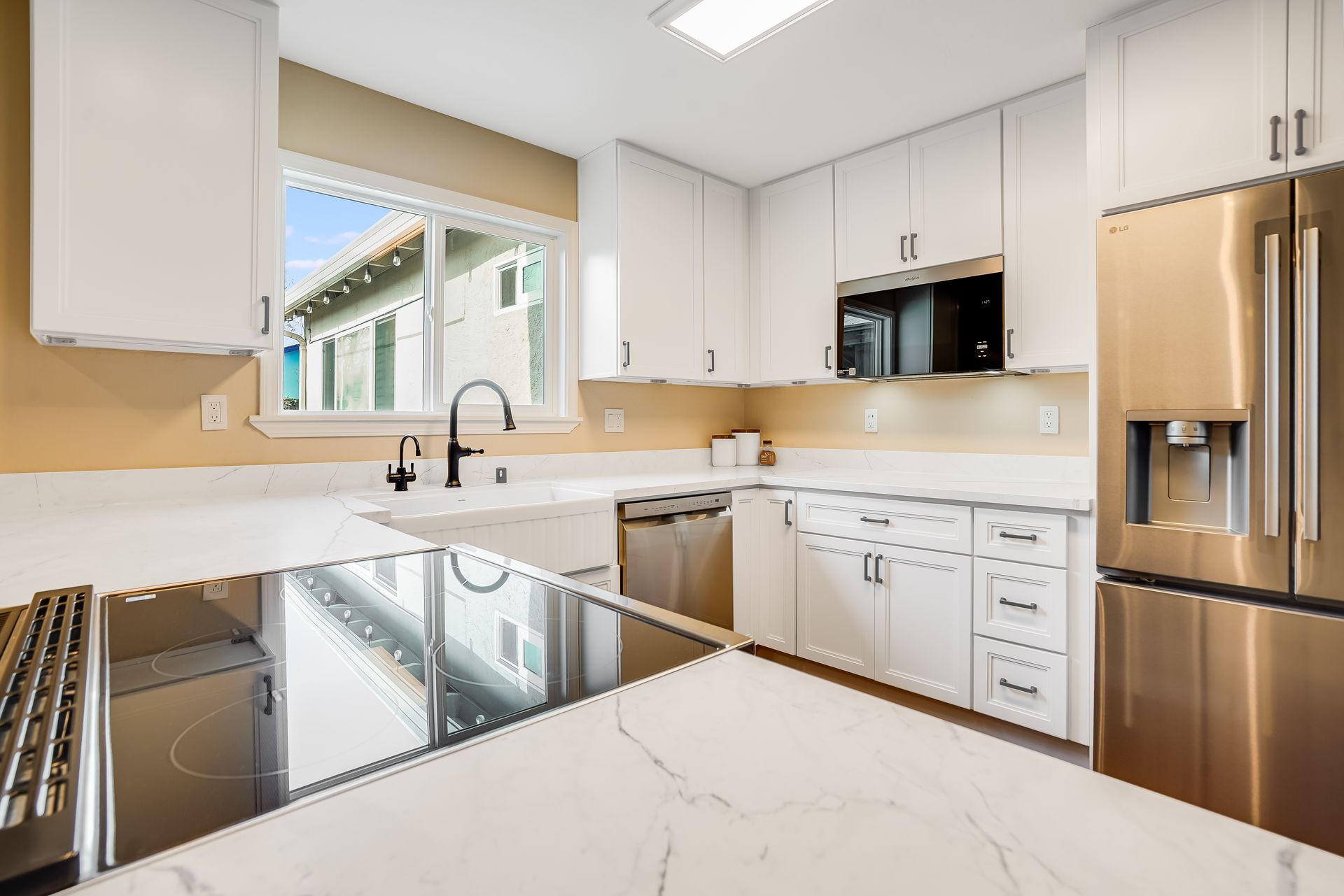 Bright modern kitchen with white cabinets, stainless steel appliances, and a large window over the sink