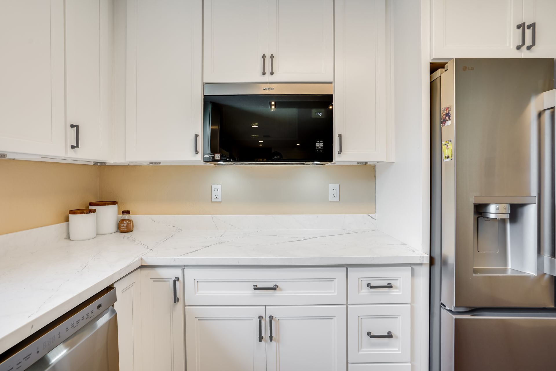 Modern white kitchen with cabinets, countertop, built-in microwave, and stainless steel refrigerator
