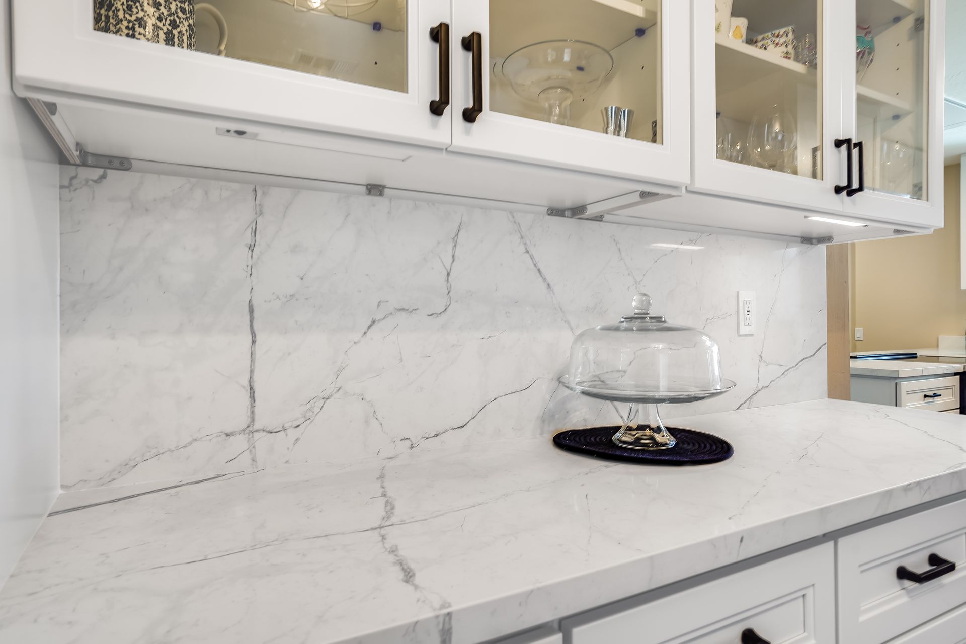 White marble kitchen countertop with matching backsplash and glass-front cabinets above