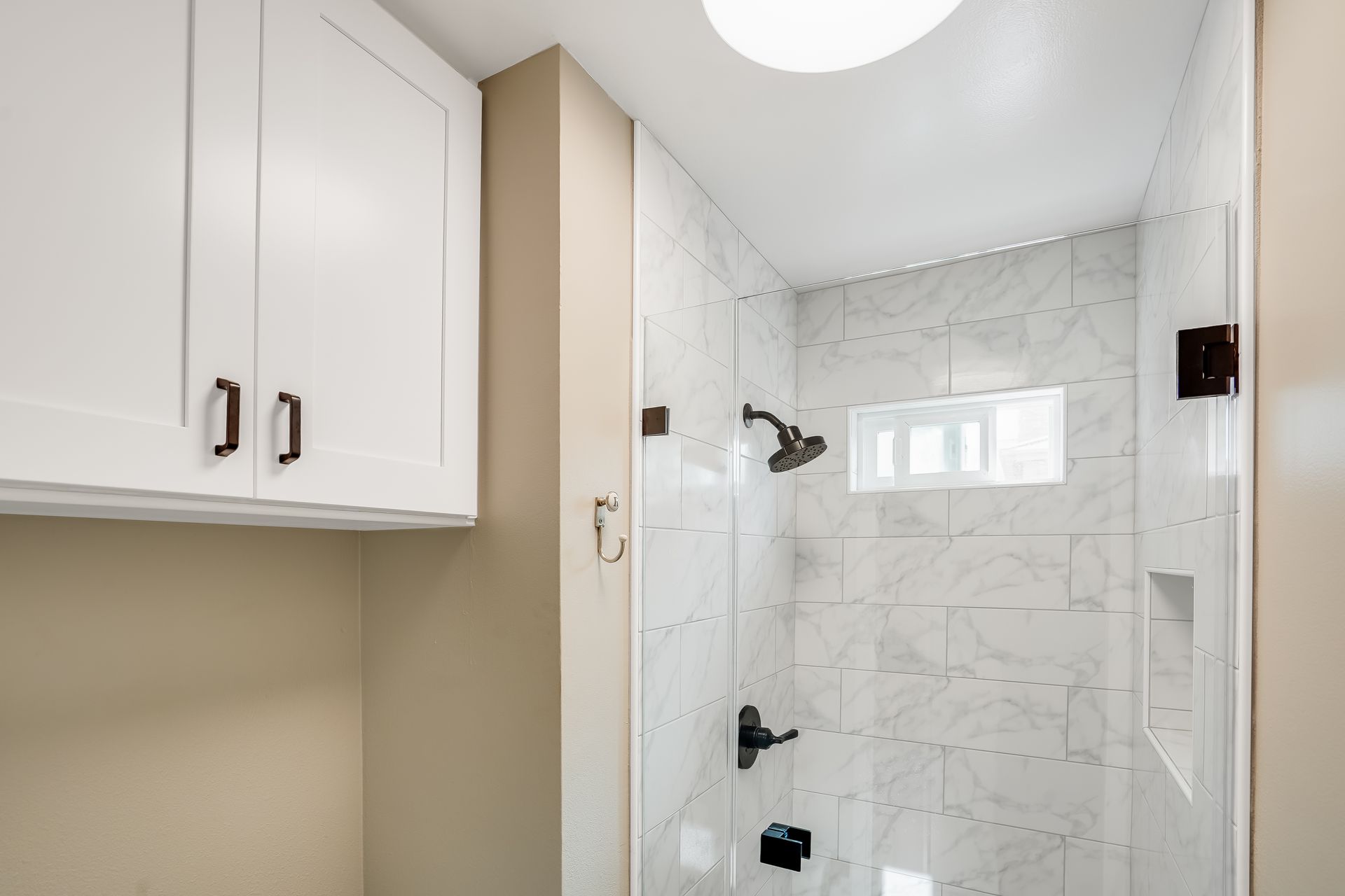 Small bathroom with white cabinets, beige walls, and a marble-tiled walk-in shower.