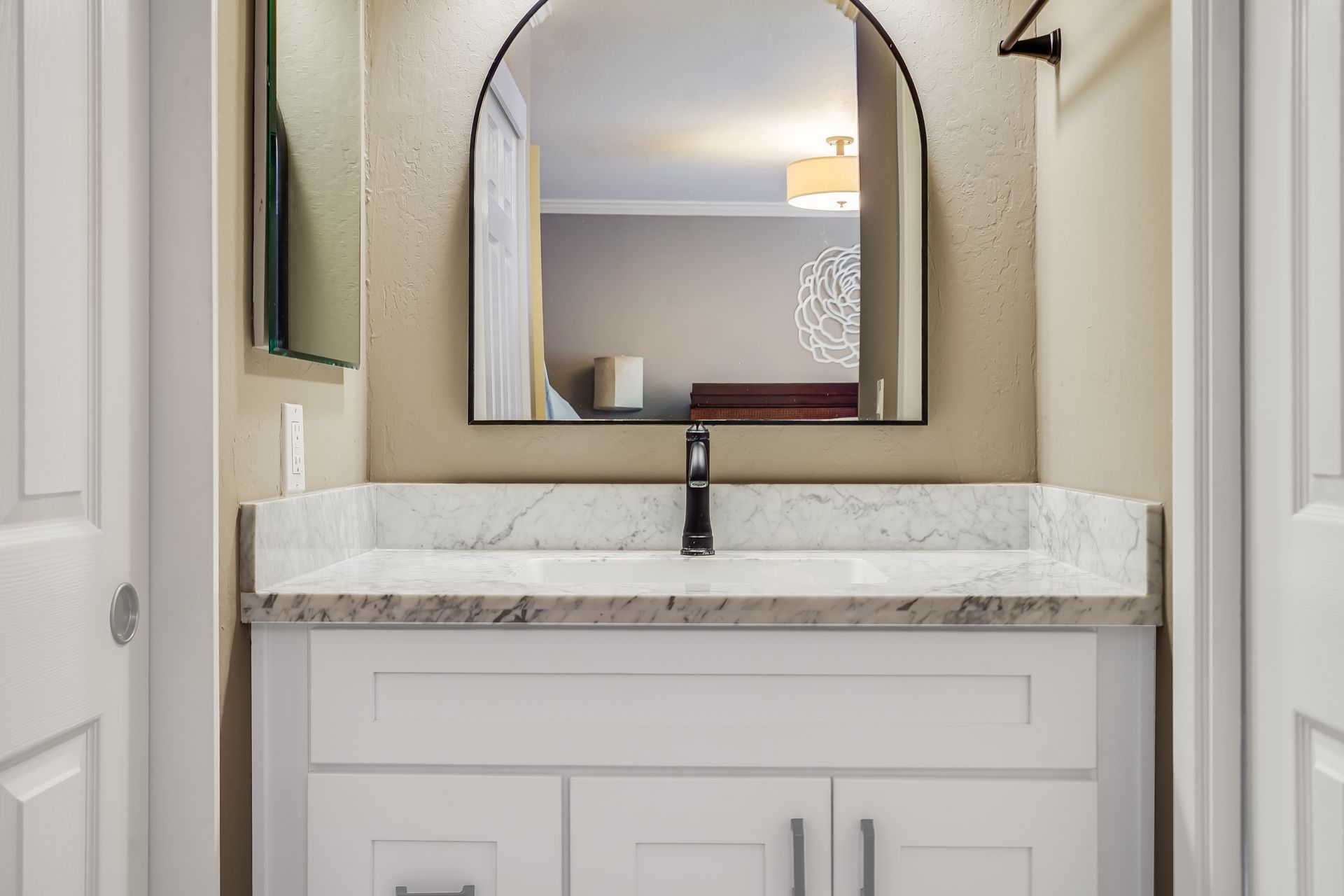 Bathroom vanity with marble countertop, black faucet, and arched mirror in a light beige room