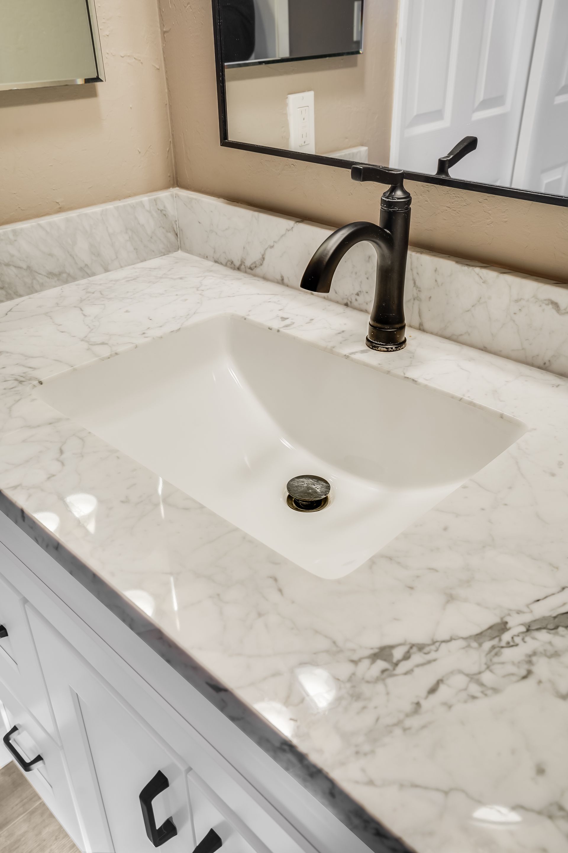 Bathroom vanity with white marble countertop, black faucet, and rectangular mirror above sink.