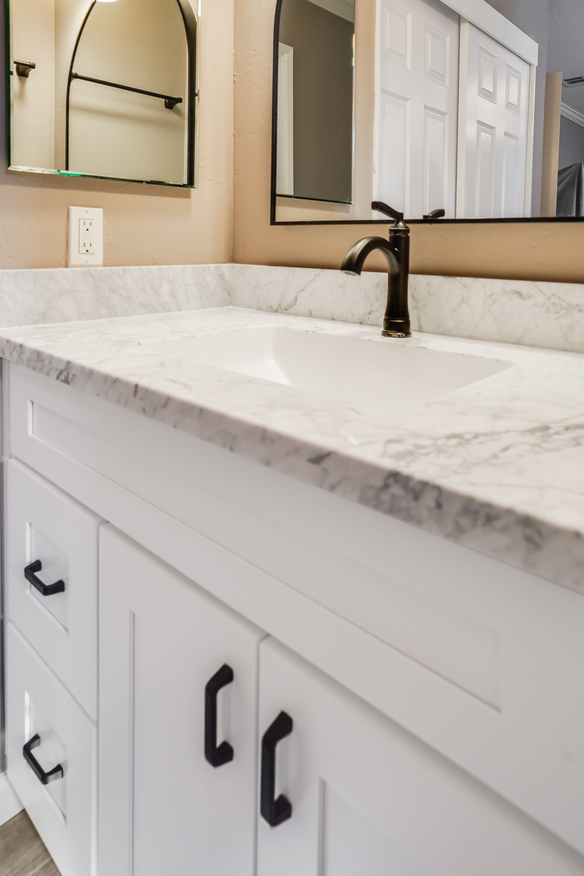 White bathroom vanity with marble countertop, undermount sink, black faucet, and mirrored cabinets