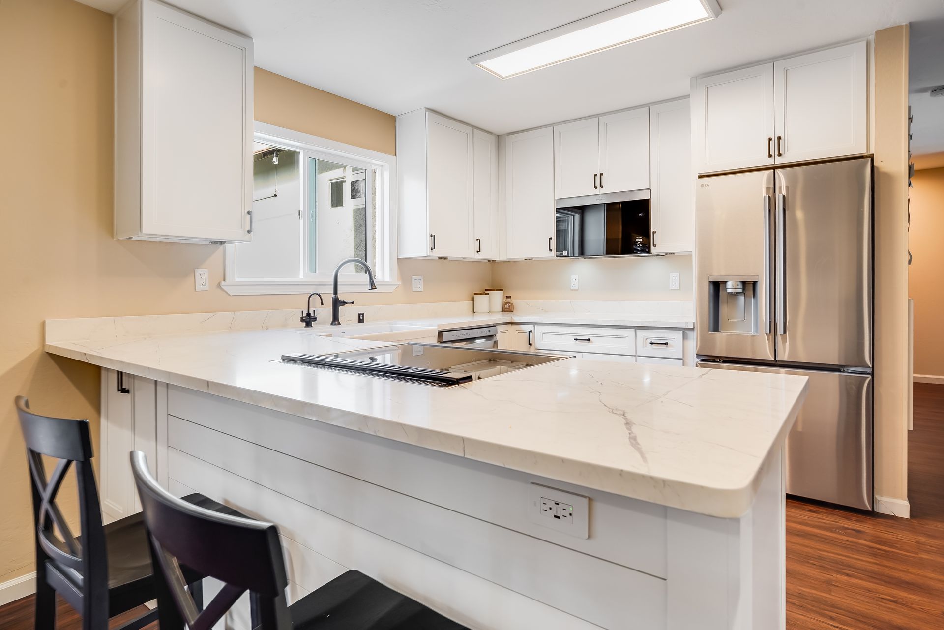 Modern white kitchen with island, stainless steel fridge, and black stools