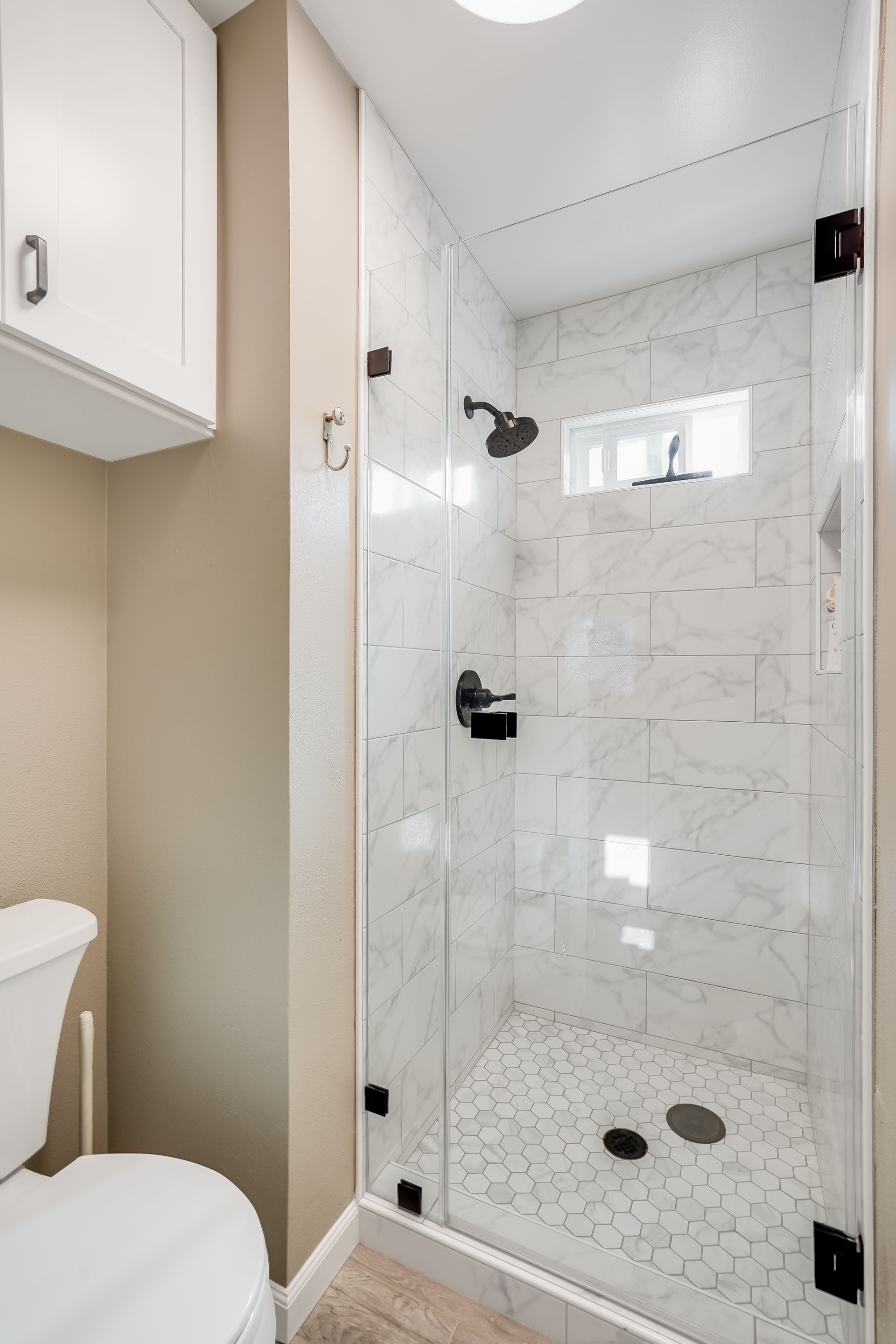 Modern bathroom shower with glass door, white tile, and chrome fixtures next to a toilet