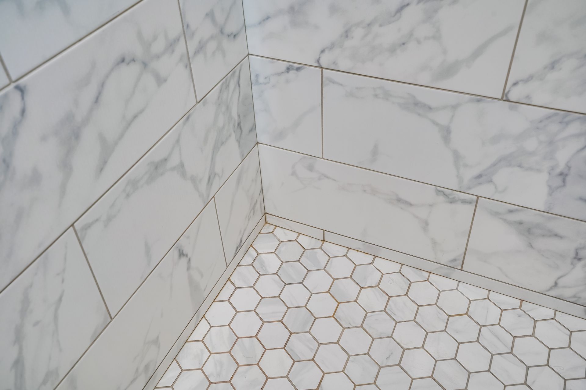 Marble-tiled shower corner with white hexagon floor tiles and wall tiles