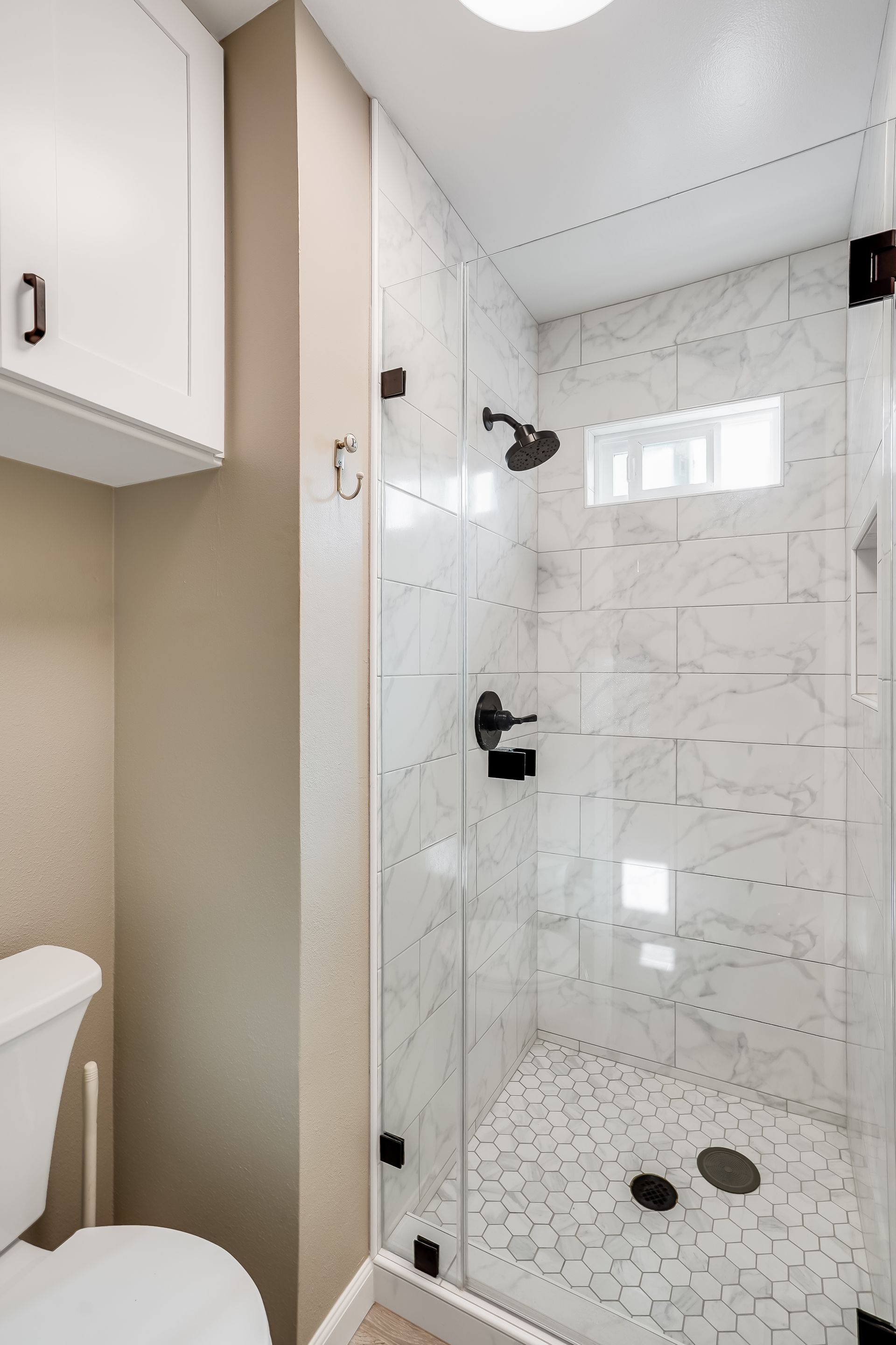 Small tiled walk-in shower with glass door, white walls, and pebble-style floor in a bathroom.