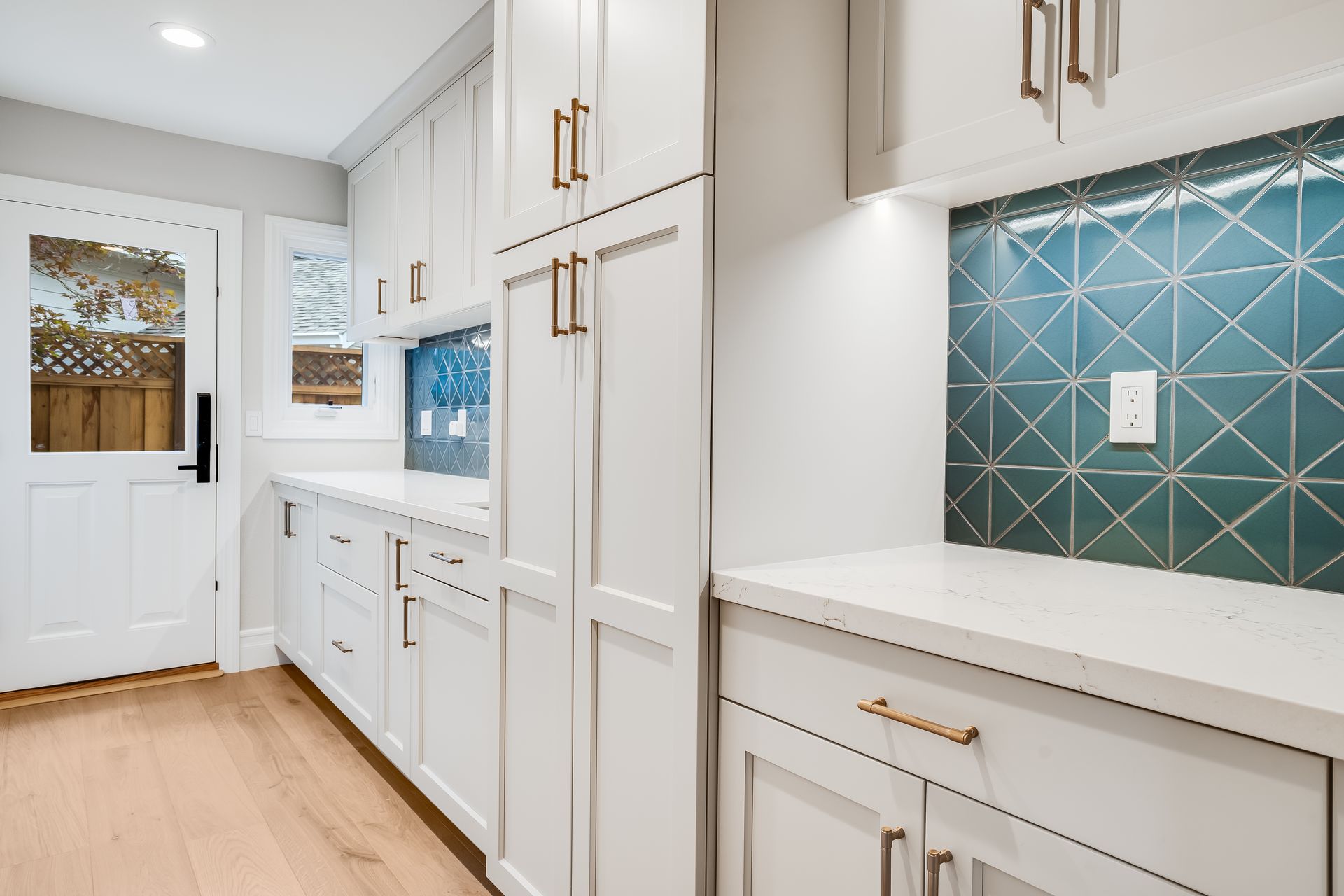 Bright laundry room with white cabinets, teal tile backsplash, and light wood flooring