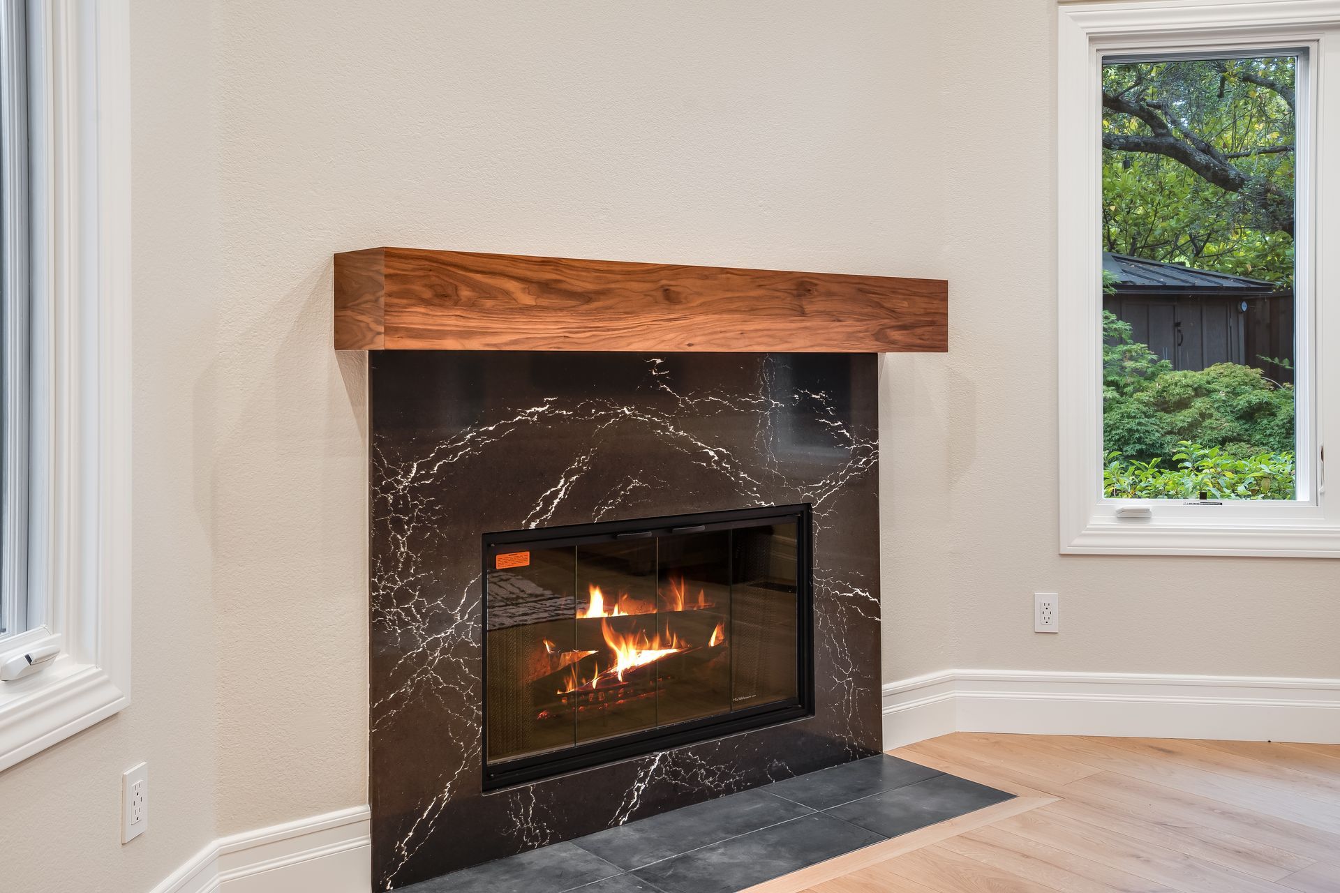 Modern living room fireplace with dark tile surround, wood mantel, and a small fire burning.