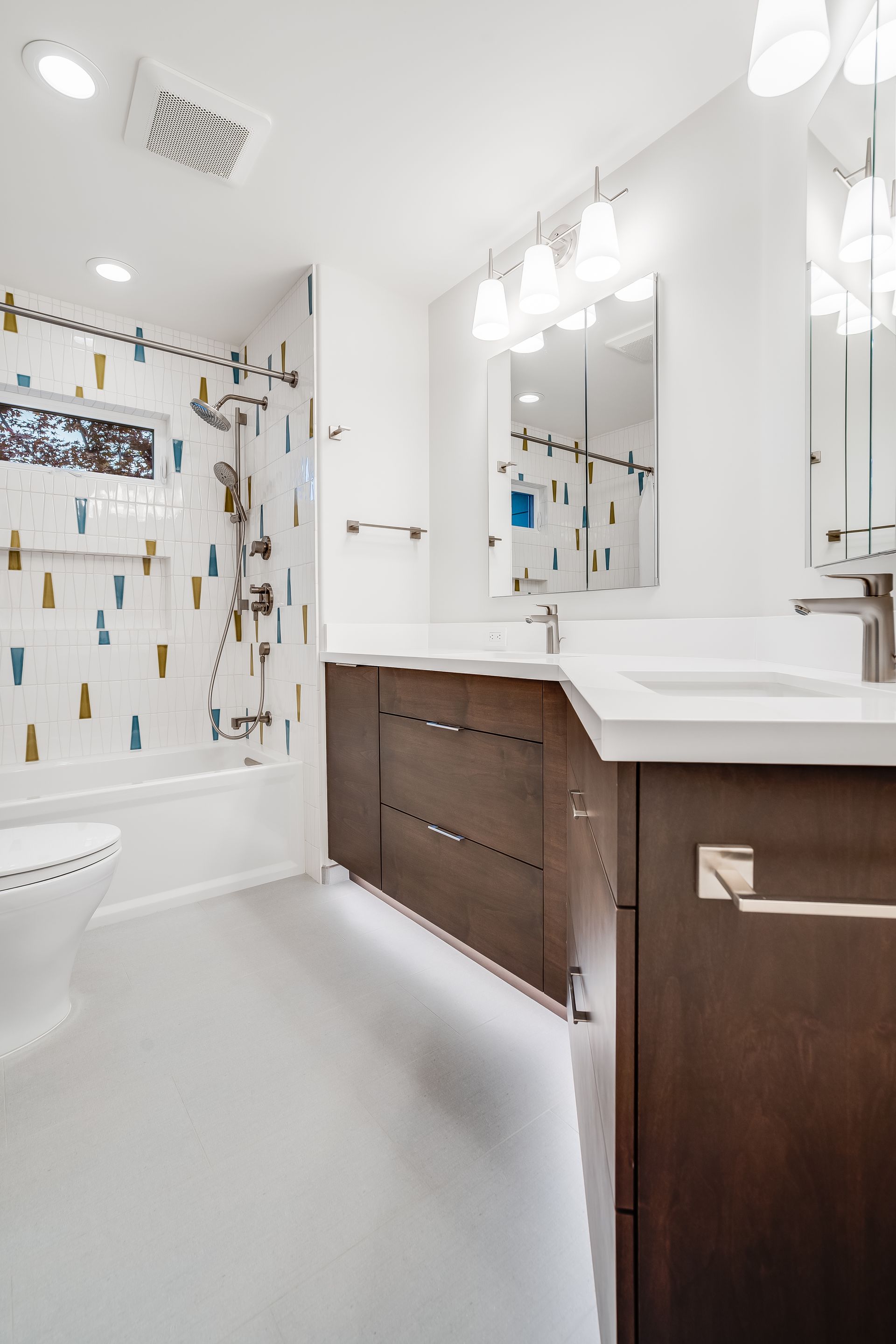 Bright white bathroom with bathtub, patterned shower curtain, and dark wood vanity with mirror lights