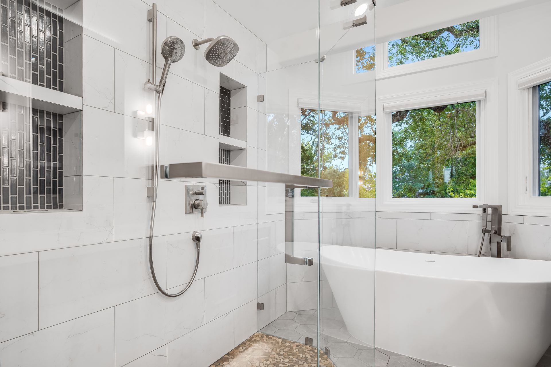 Bright white bathroom with walk-in shower, freestanding tub, and large windows overlooking greenery