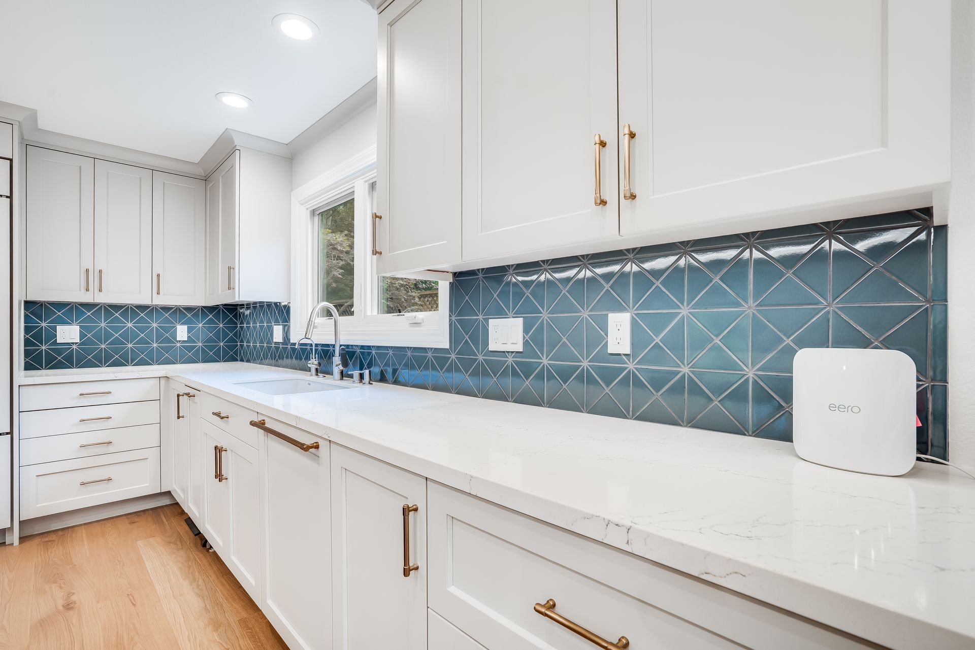 Bright white kitchen with blue tile backsplash, gold hardware, and long countertop.