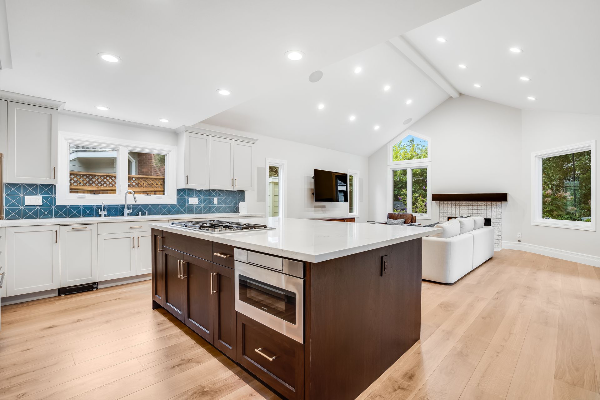 Bright modern kitchen with white cabinets, dark island, wood floors, and large windows