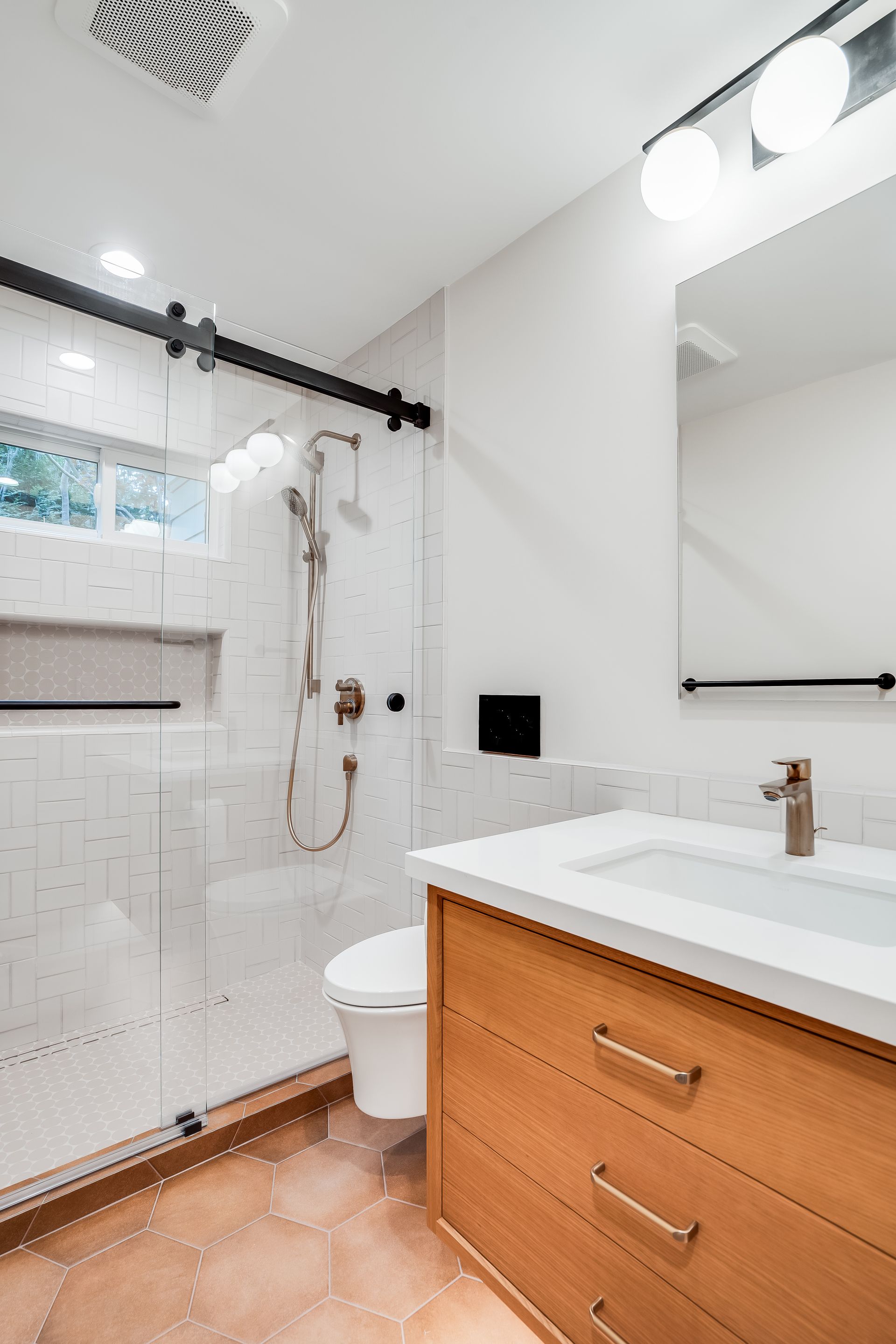 Bright modern bathroom with a glass shower, white sink, wood vanity, and toilet.
