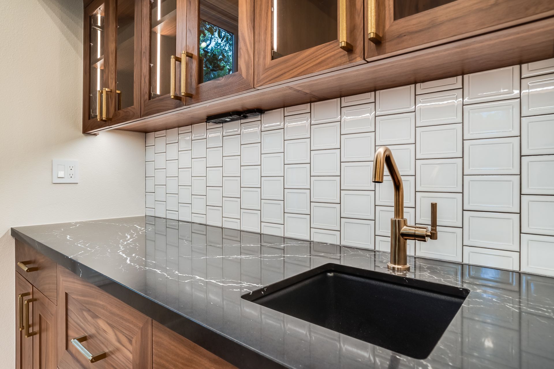 Modern kitchen countertop with black sink, gold faucet, and white tiled backsplash