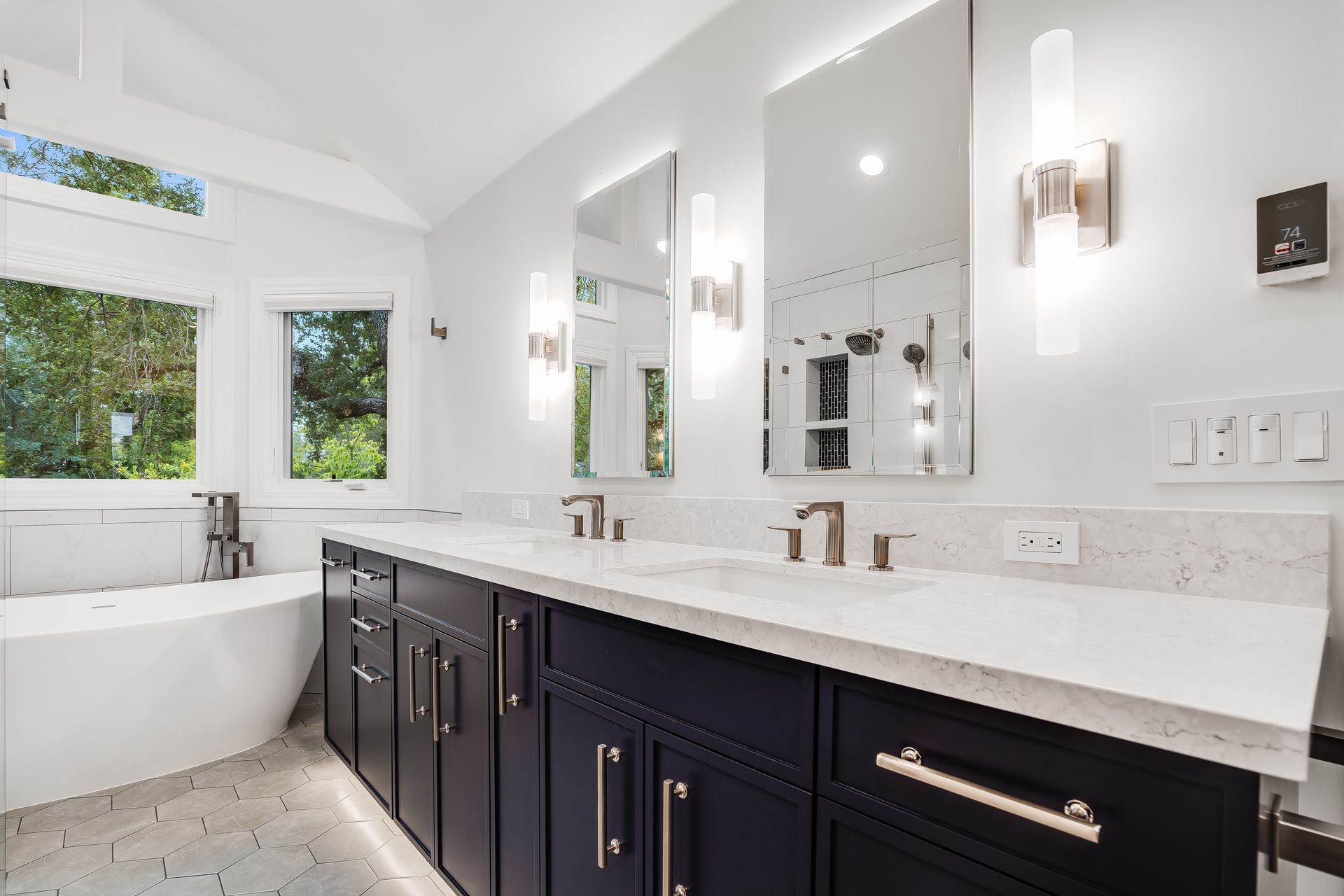 Bright modern bathroom with double vanity, large mirrors, white marble, and a soaking tub by windows