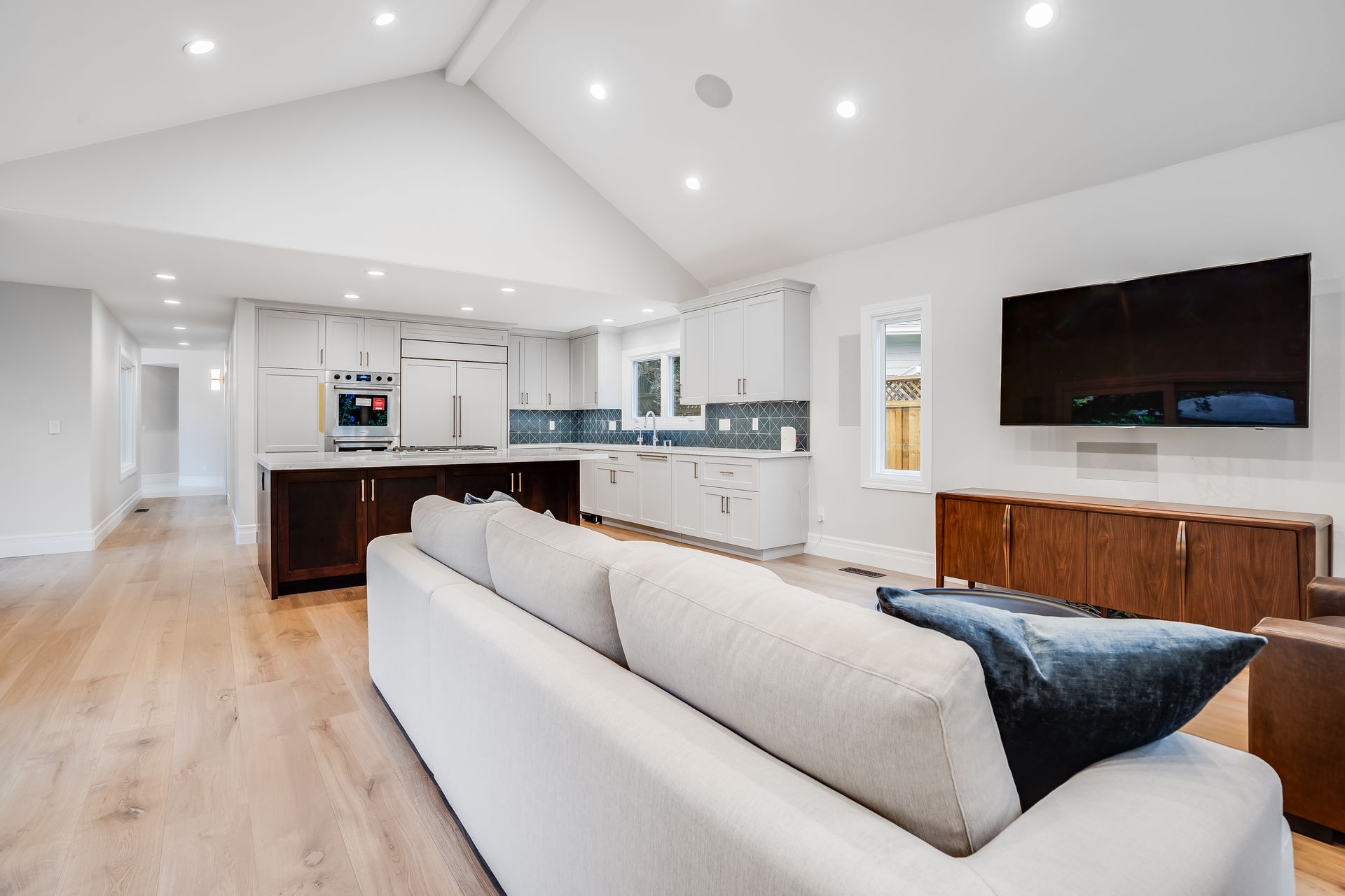 Bright open-concept living room with white walls, wood floors, gray sofa, and kitchen island under vaulted ceilings