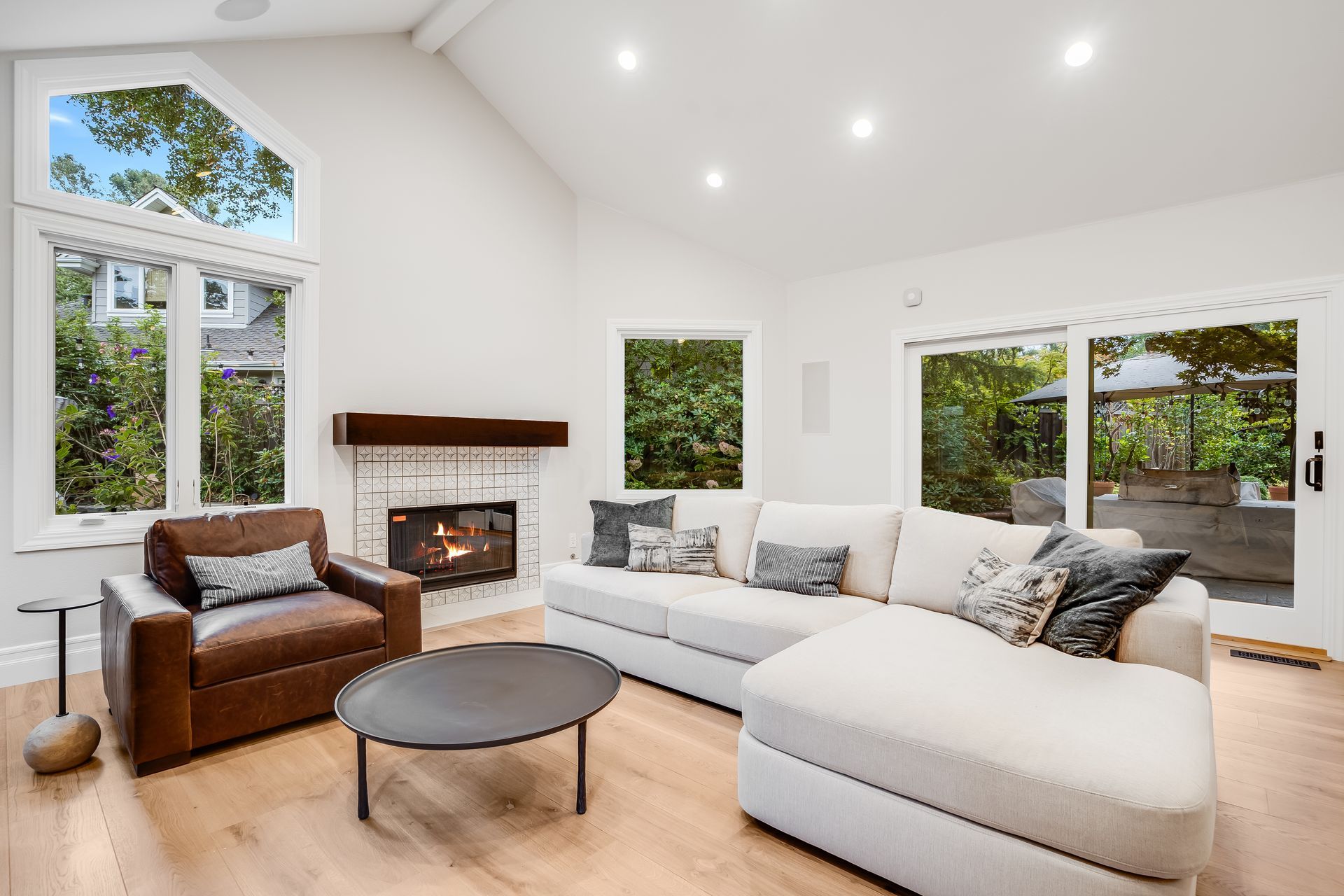 Bright modern living room with white sectional sofa, fireplace, and large windows overlooking greenery