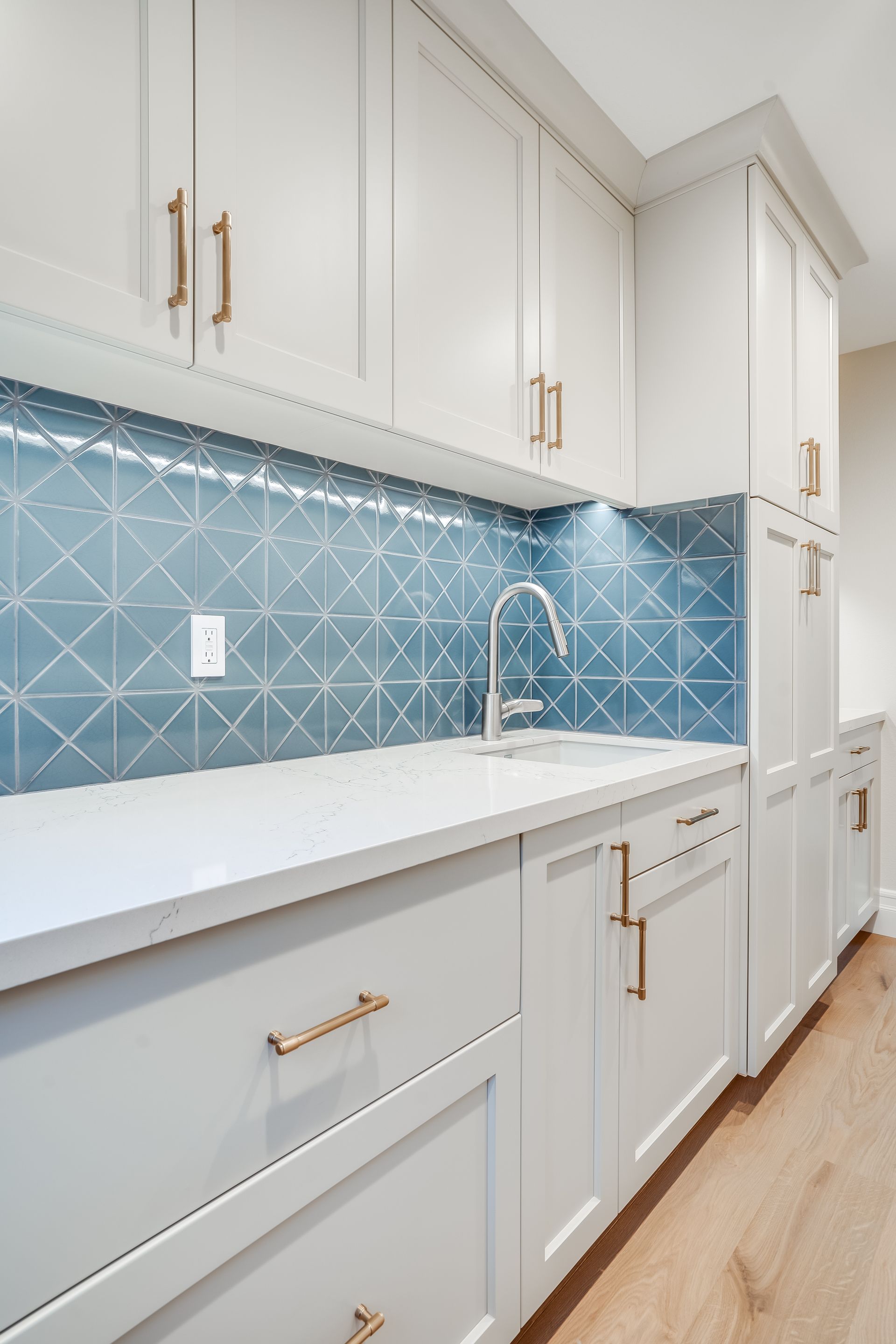 Bright white kitchen with blue patterned backsplash, brass cabinet pulls, sink, and light wood floor